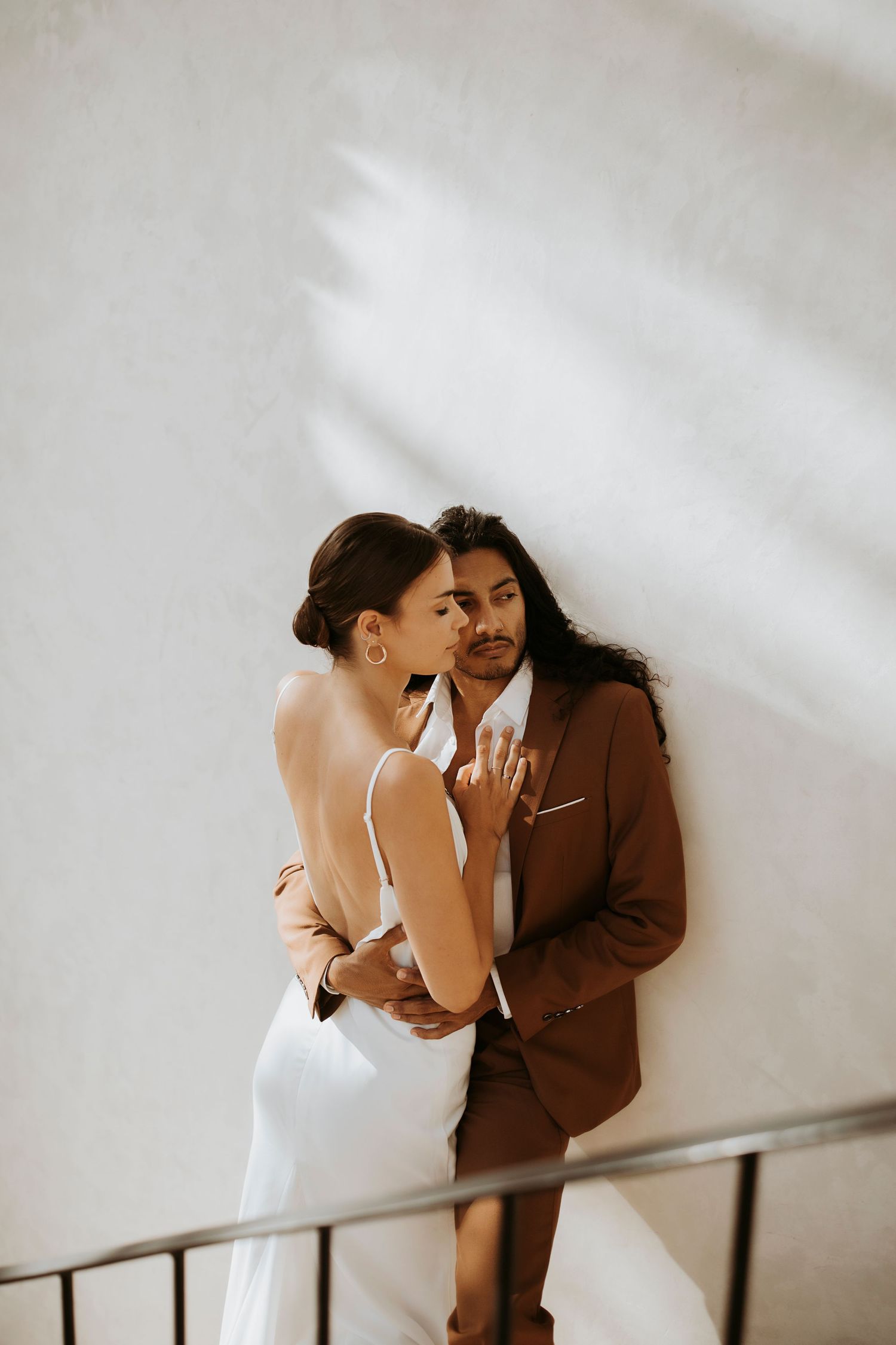 Intimate couple moment against white wall with dramatic shadows.