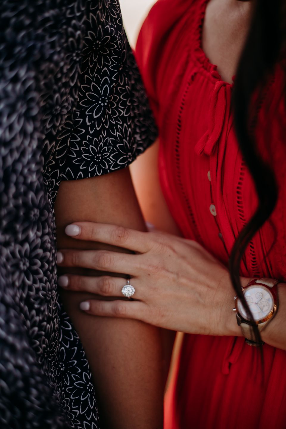 Close-up of hands showing an engagement ring against red and navy patterned clothing.