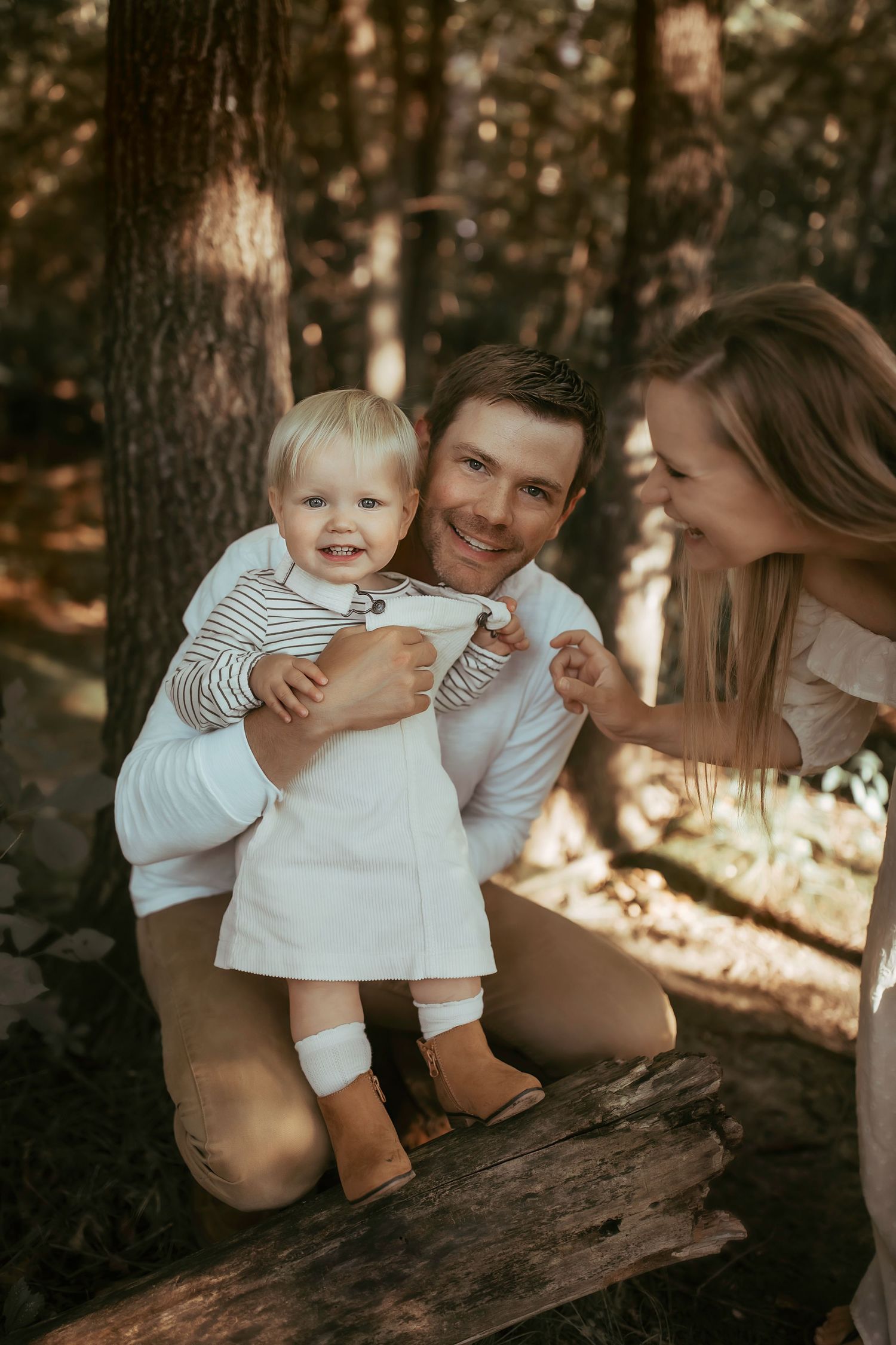 A happy family moment captured in warm sunlight as they stand together on a fallen log in the woods.