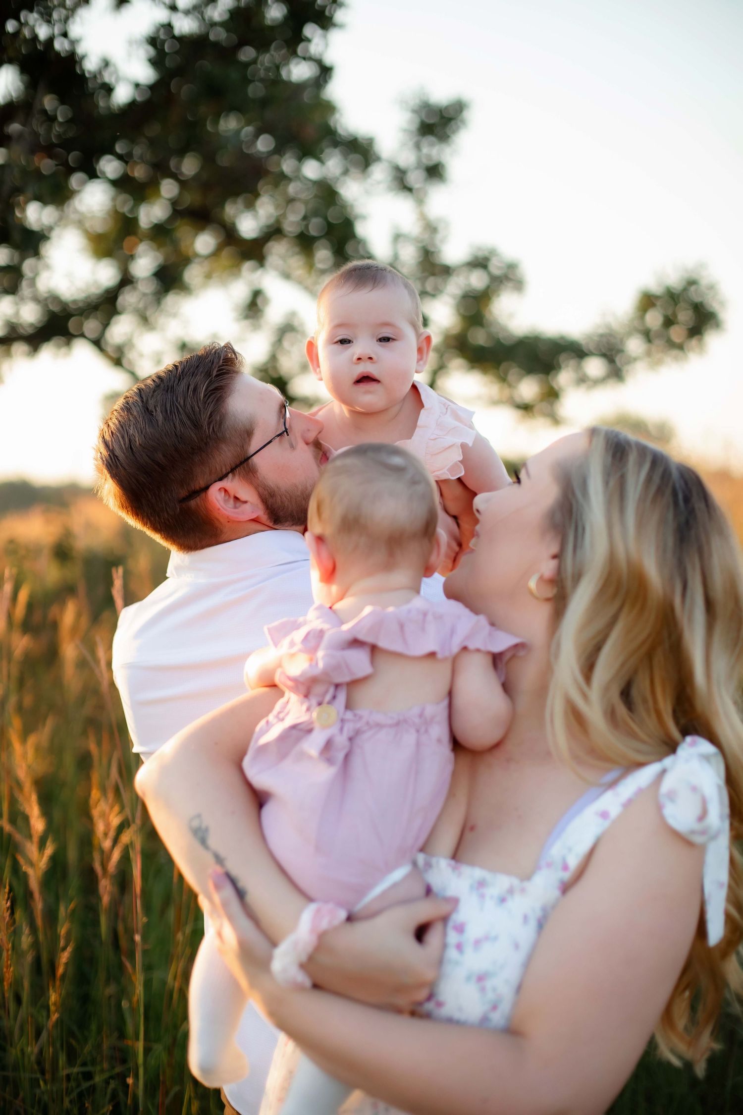 Parents sharing tender moment with twin babies during sunset photo session.