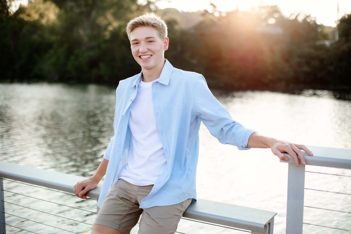 Casual summer portrait by water at sunset wearing light blue button-down shirt.