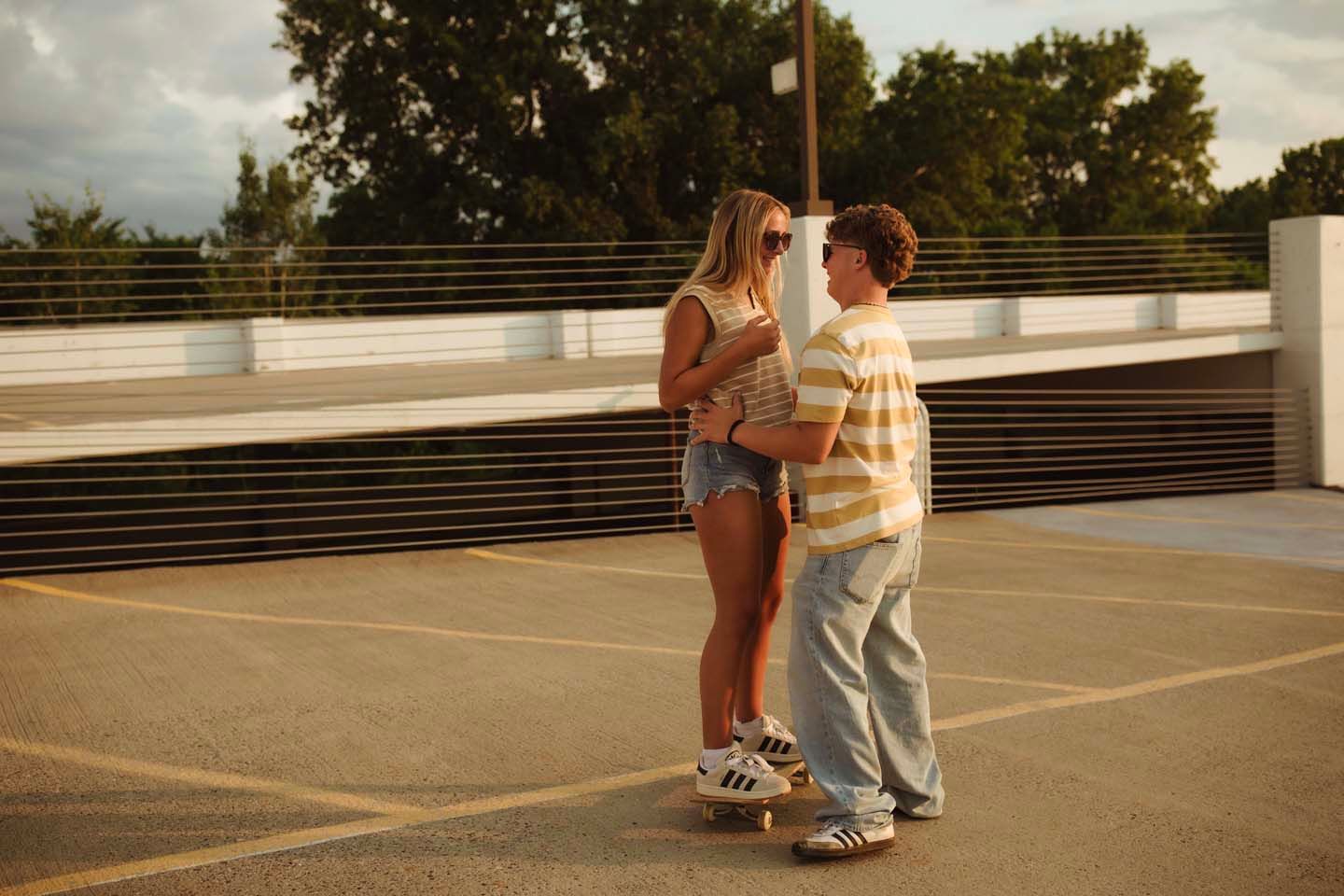 Teen couple holding hands on a rooftop parking lot at golden hour sunset.