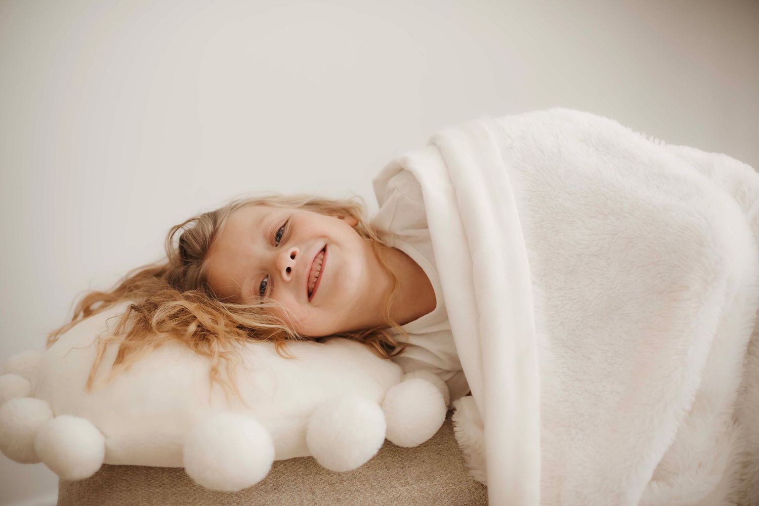 Person wrapped in soft white bedding lies peacefully against light colored pillows and blankets.