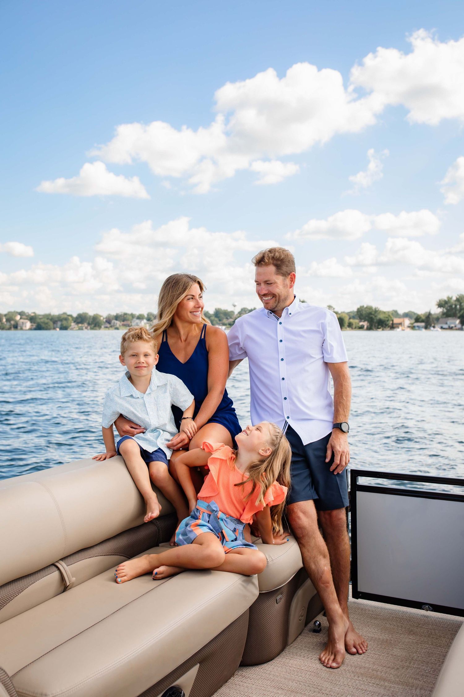 Family enjoying a sunny day together on a pontoon boat with blue water and clouds in the background.