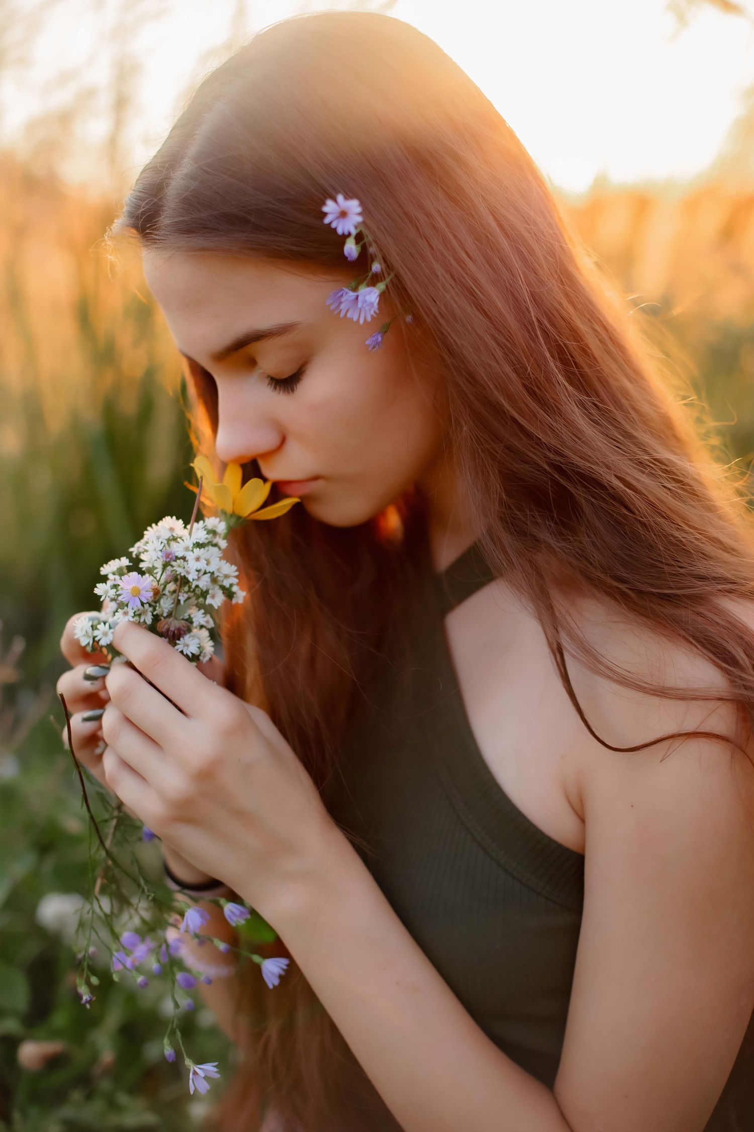 Romantic portrait smelling wildflowers with delicate purple blooms in hair at golden hour.