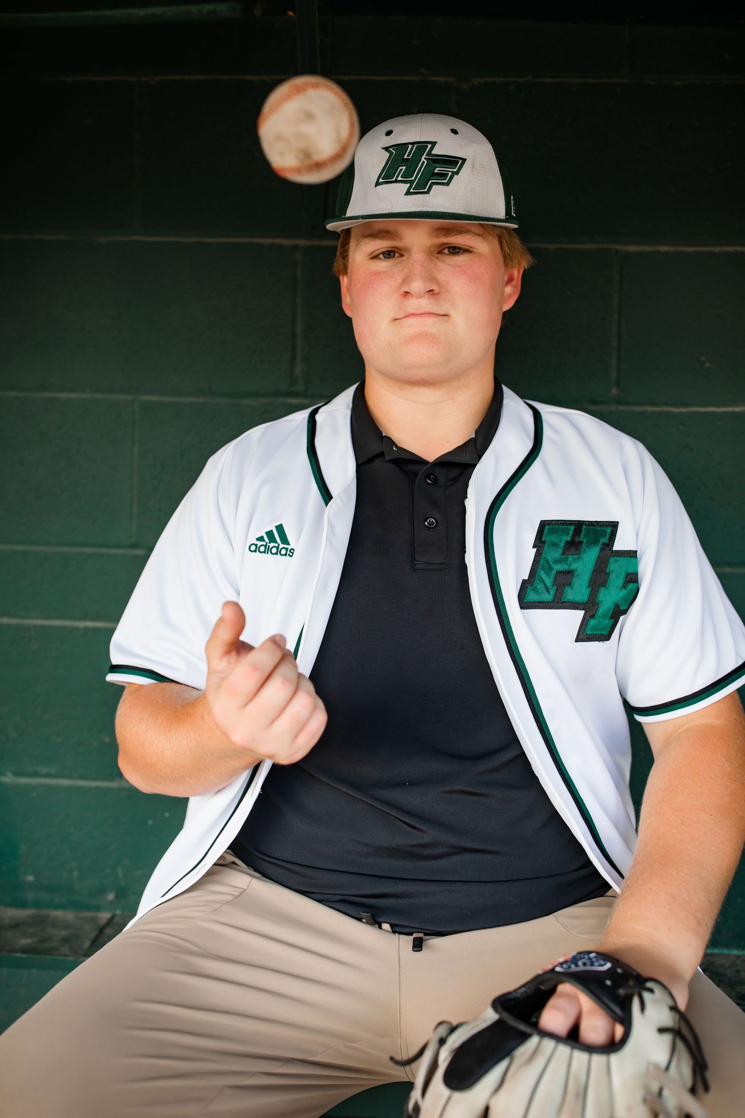 Baseball player wearing team jersey and hat holding glove in dugout.