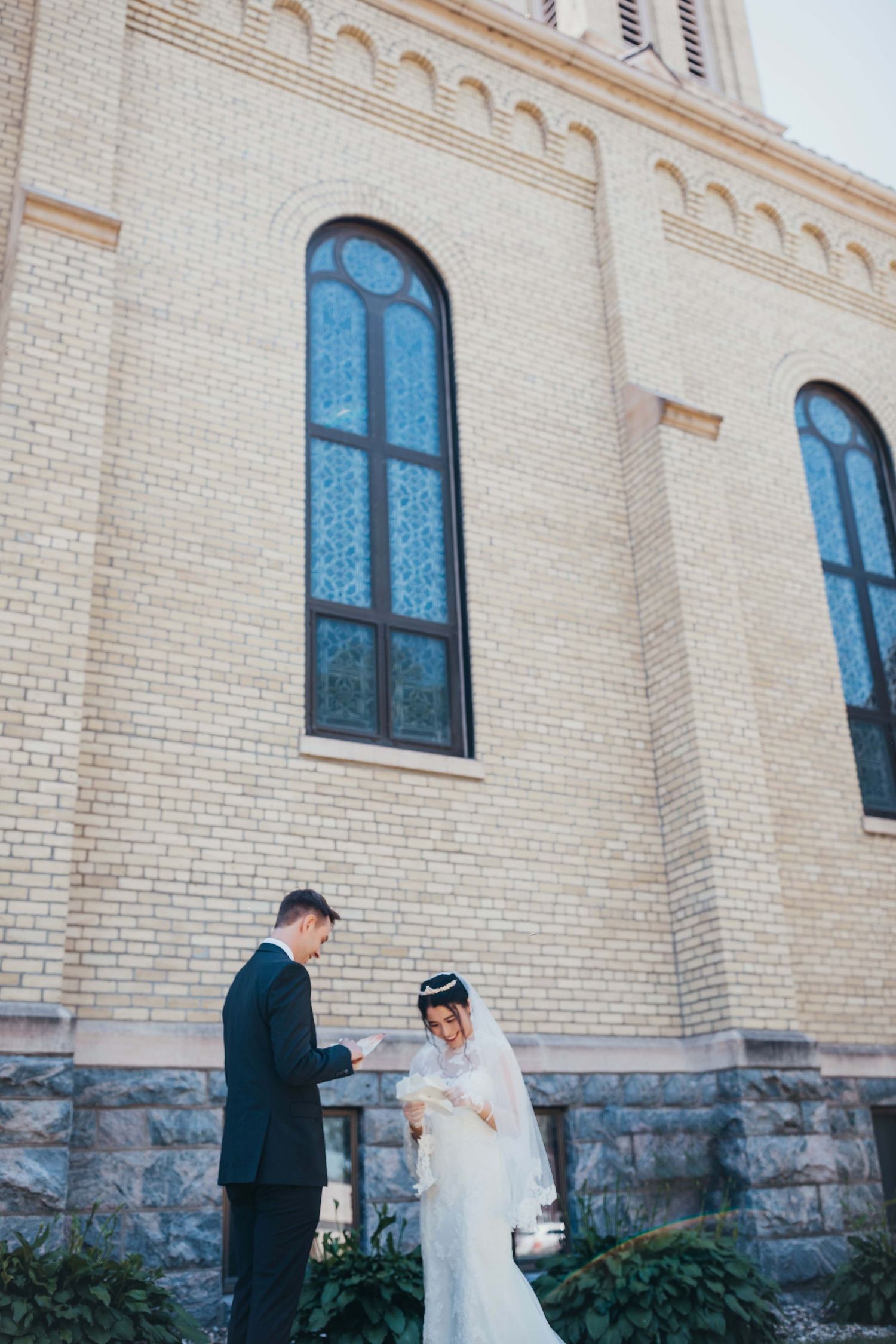 Wedding couple standing by historic church with tall arched windows.