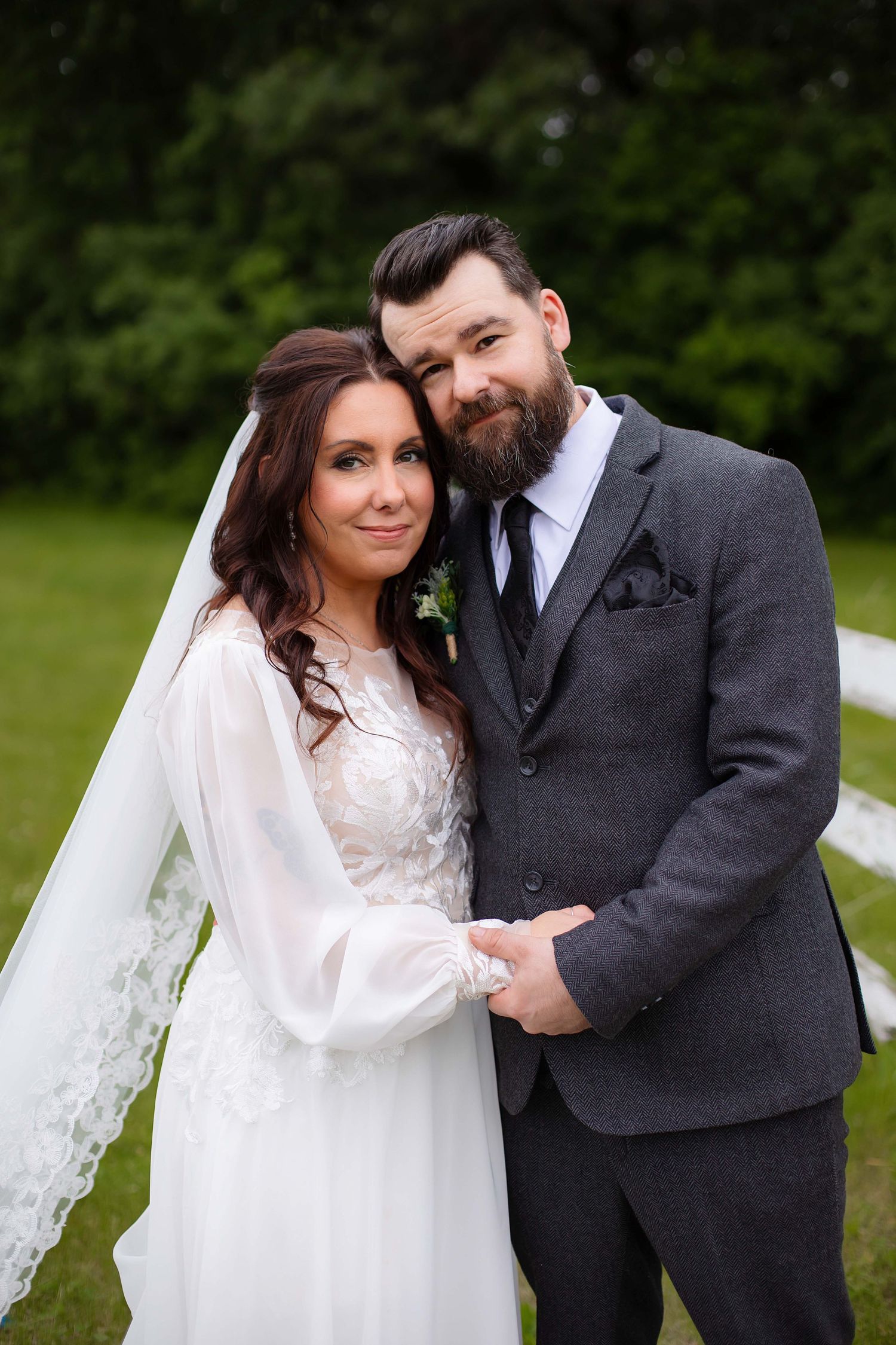 A romantic wedding portrait in a lush green outdoor setting.