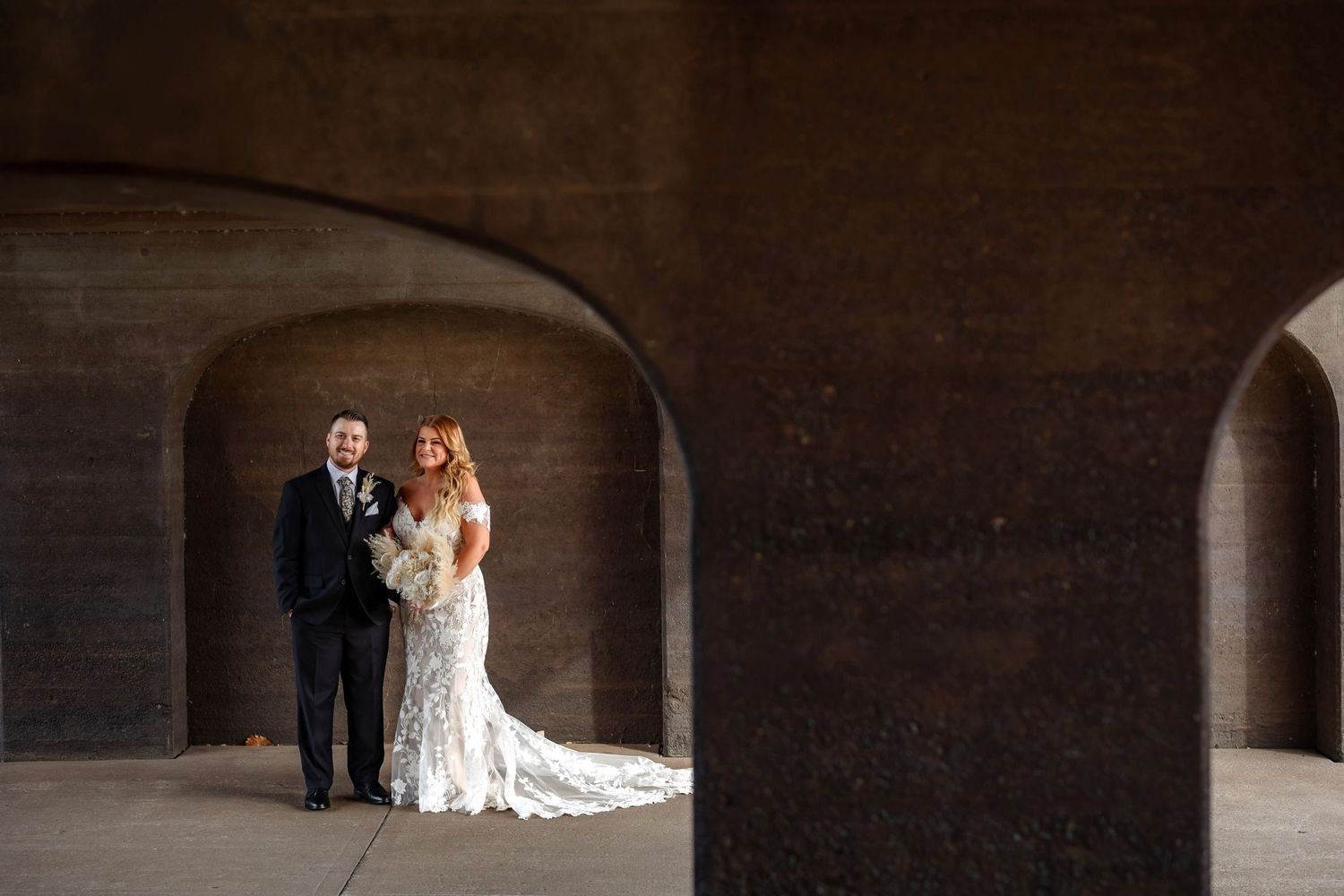 A wedding couple framed within a dramatic stone archway in moody lighting.