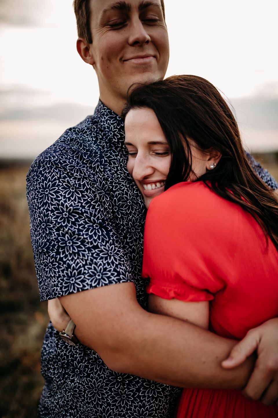 Joyful embrace between couple in navy patterned shirt and vibrant red dress outdoors.
