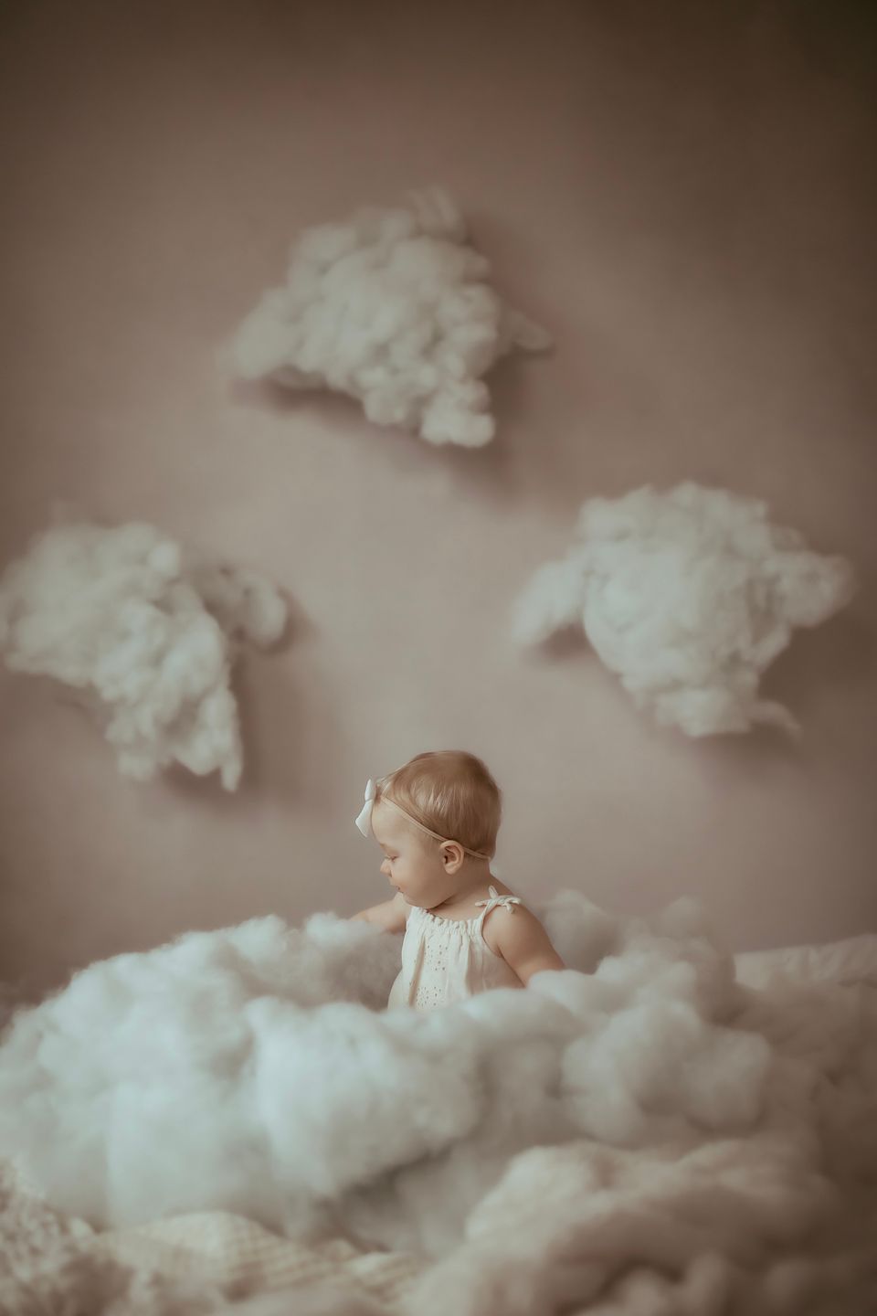 Dreamy portrait with baby surrounded by cloud decorations in sepia tones.