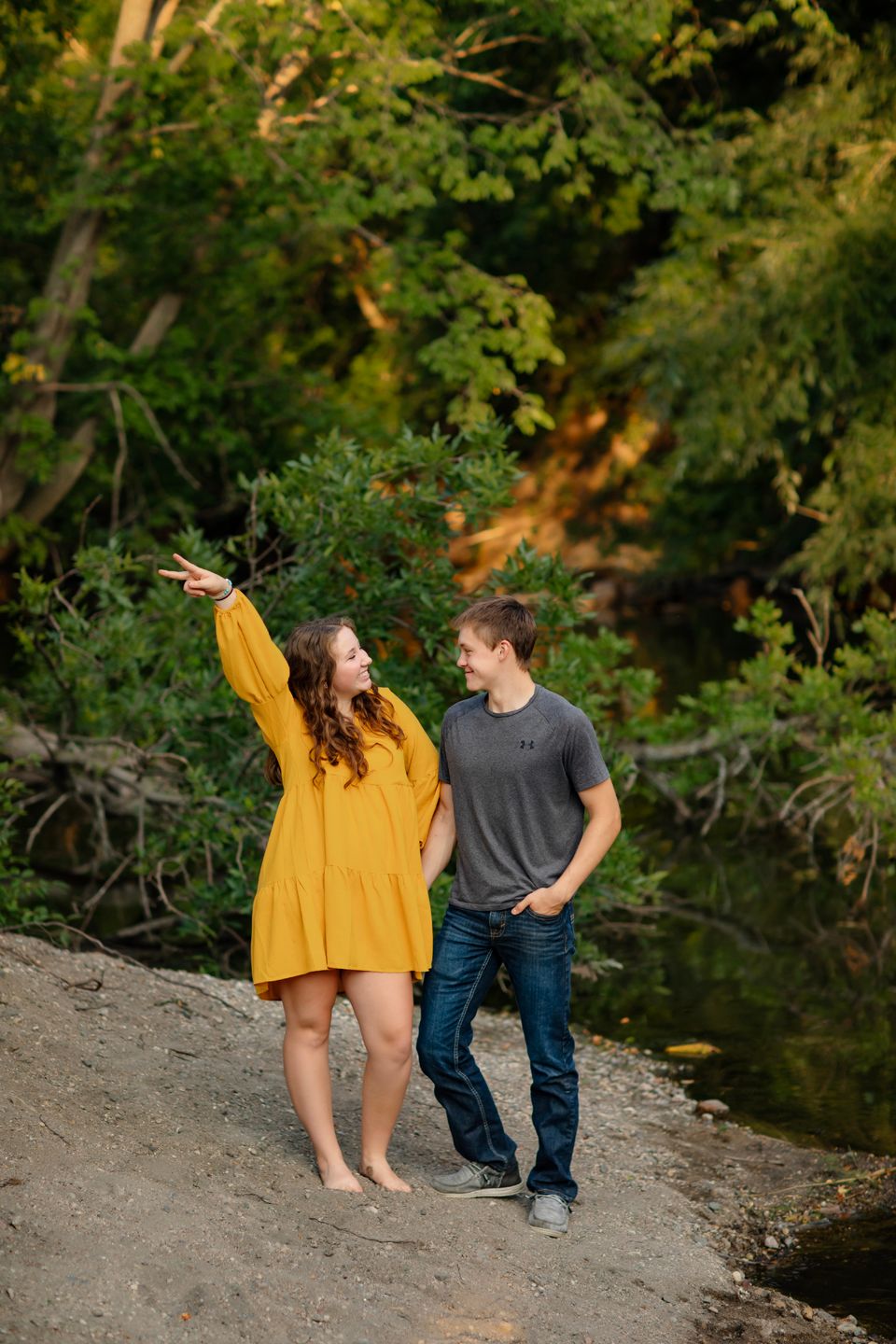 Couple standing together near a river bank during sunset.