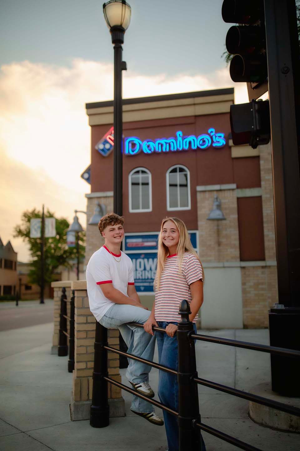 Young couple posing together outside a Dominos Pizza restaurant at sunset.