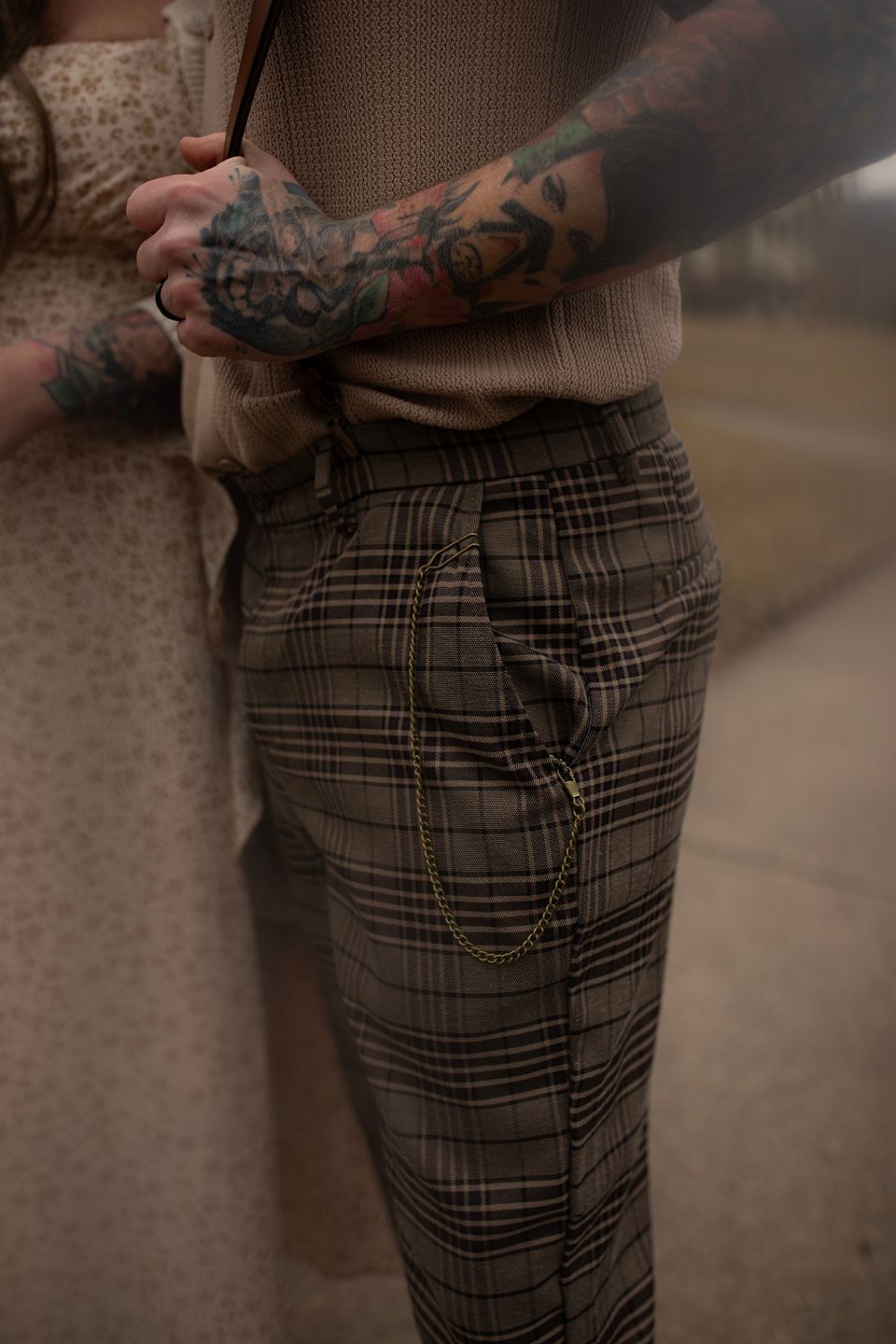 Detailed view of plaid trousers and tattooed arms showing casual fashion style.
