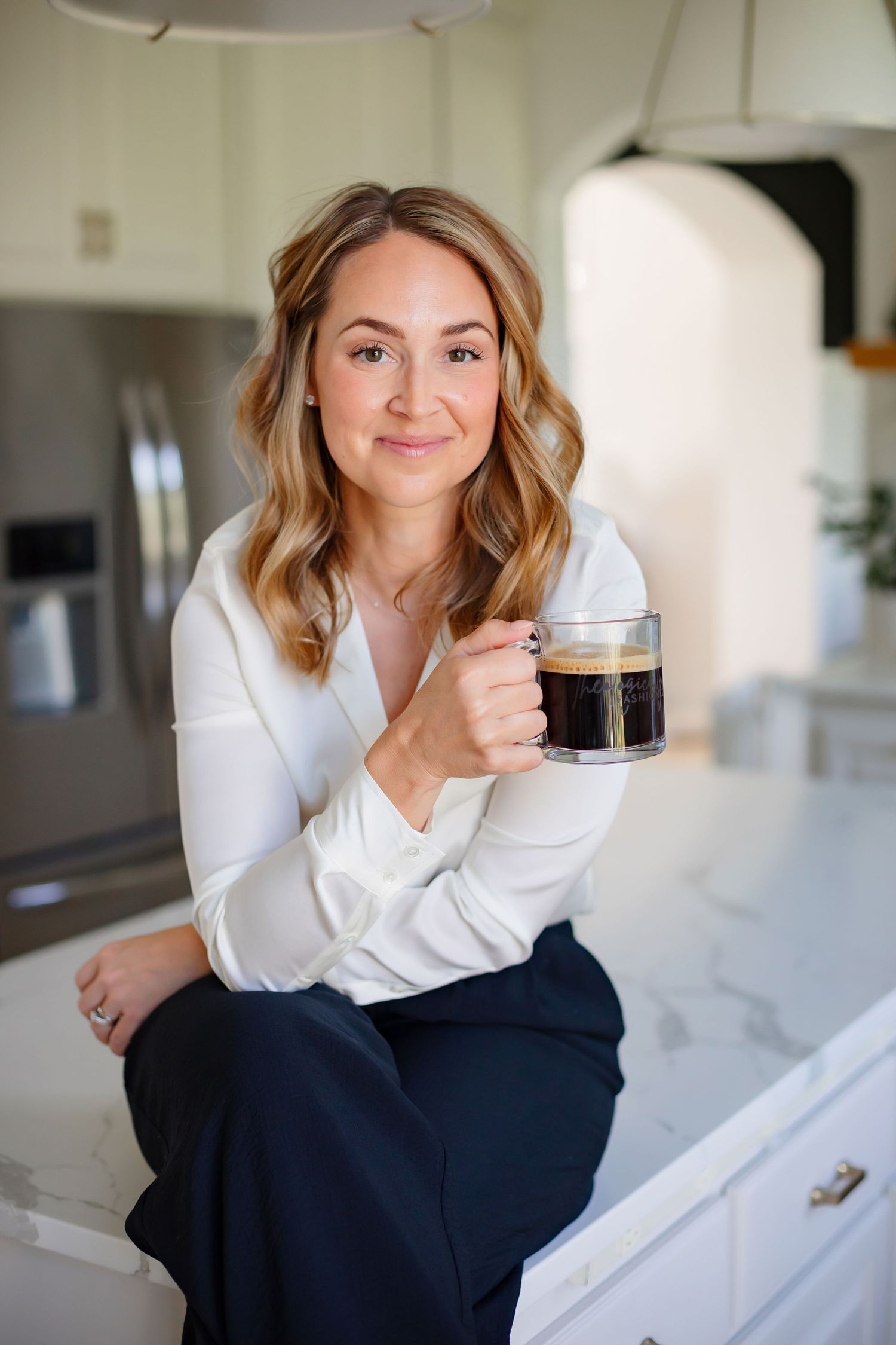 Bright kitchen setting with marble countertop and coffee in hand.