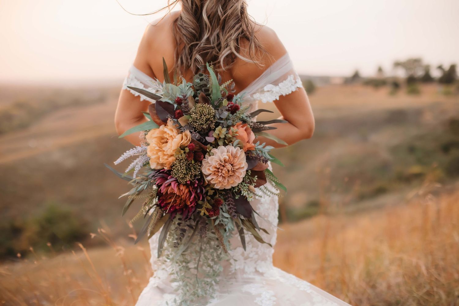 A detailed shot of a rustic wedding bouquet with peach dahlias and wildflowers against a lace dress.