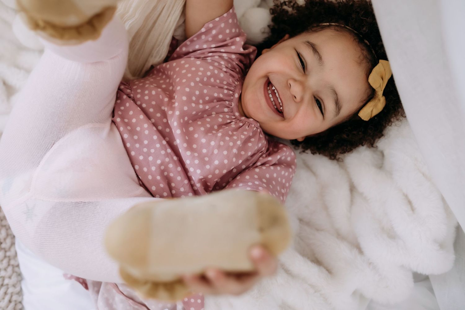A joyful toddler laughs while lying on soft white bedding.