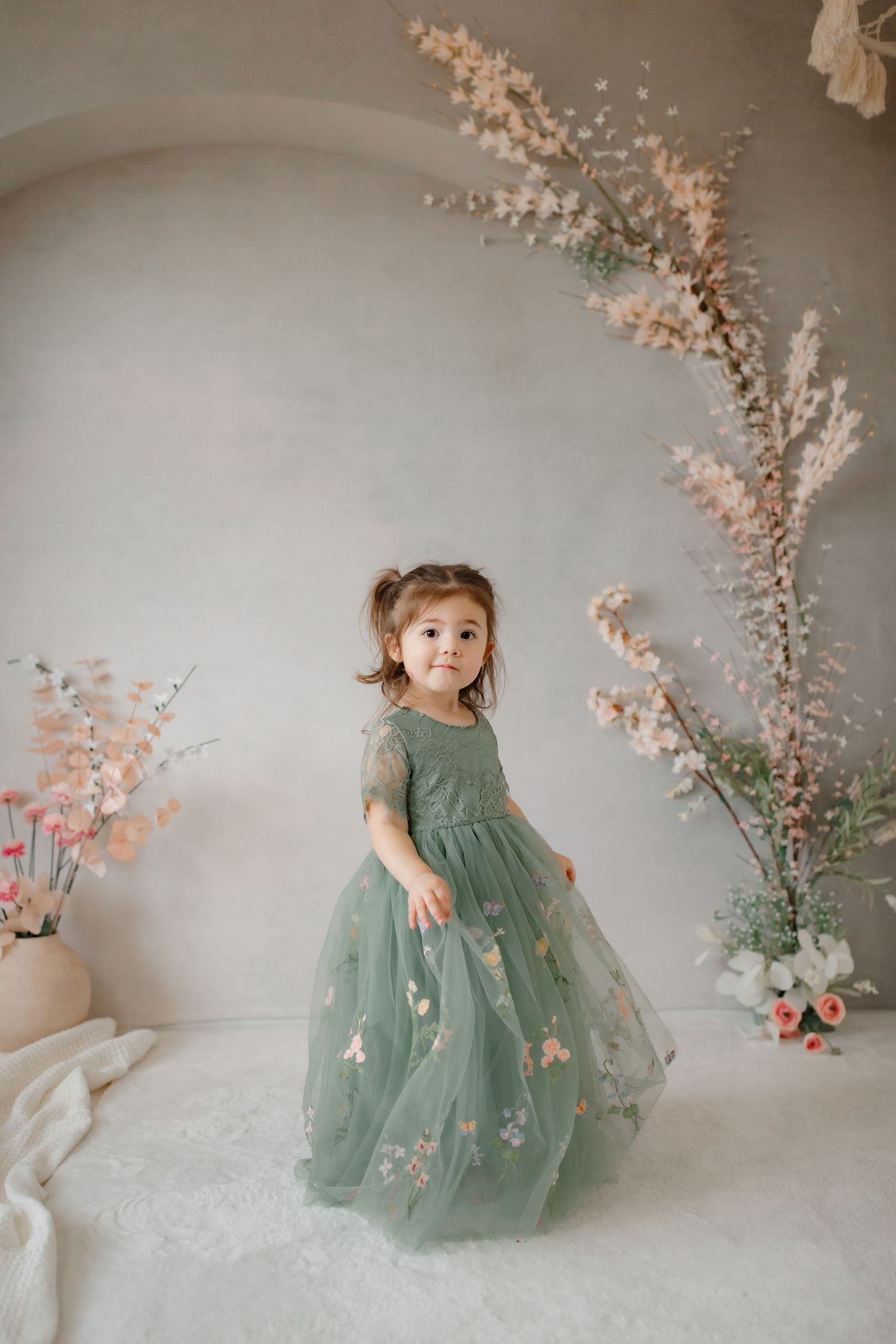 A whimsical scene with a sage green floral dress against a romantic backdrop with pink flowers.