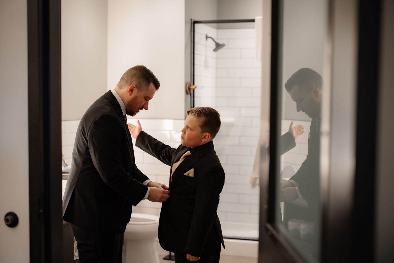 Two people preparing formal attire in a minimalist interior hallway.