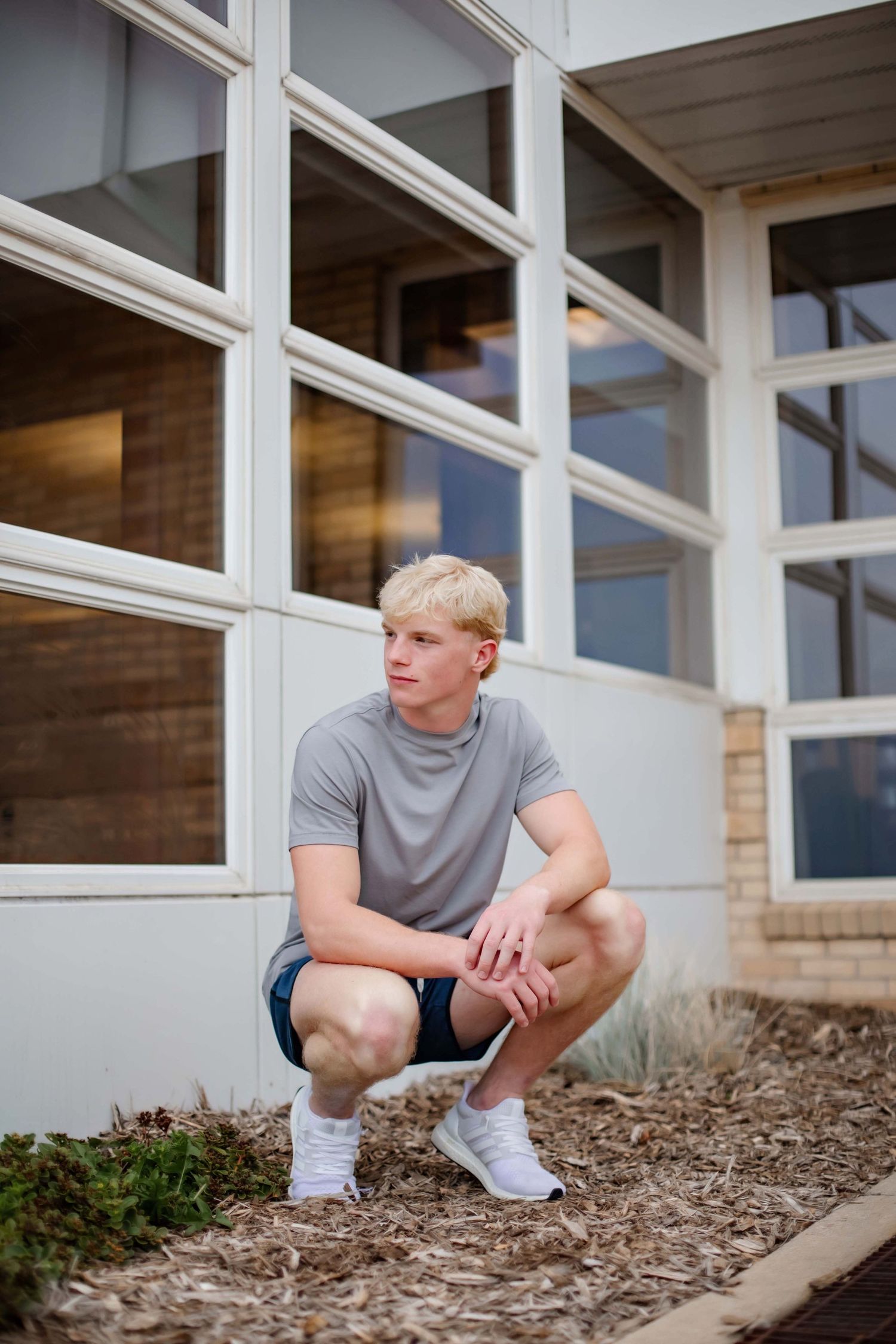 Athletic pose in grey t-shirt and shorts by modern building with glass windows.