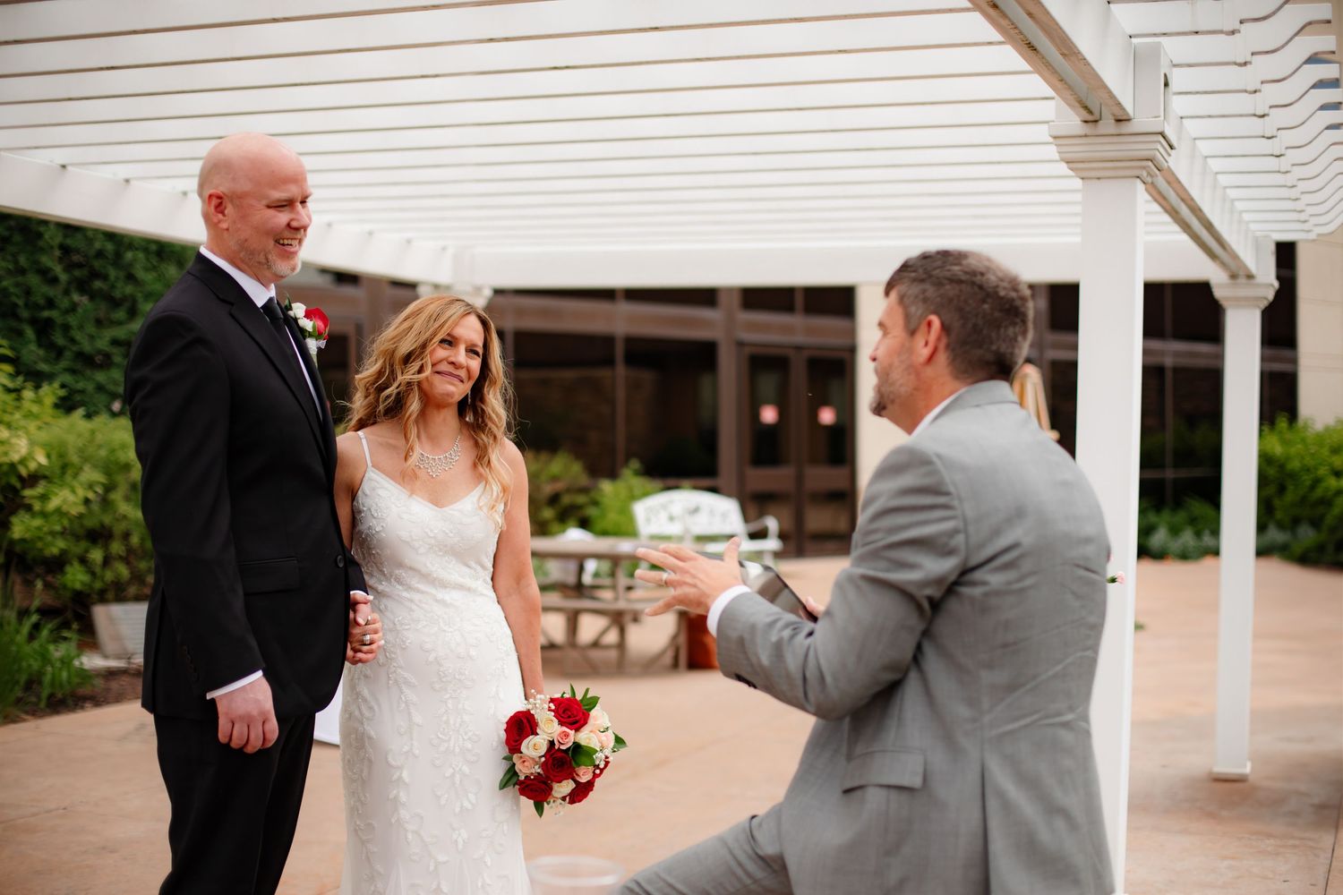 Wedding ceremony participants gather under white pergola during outdoor celebration.