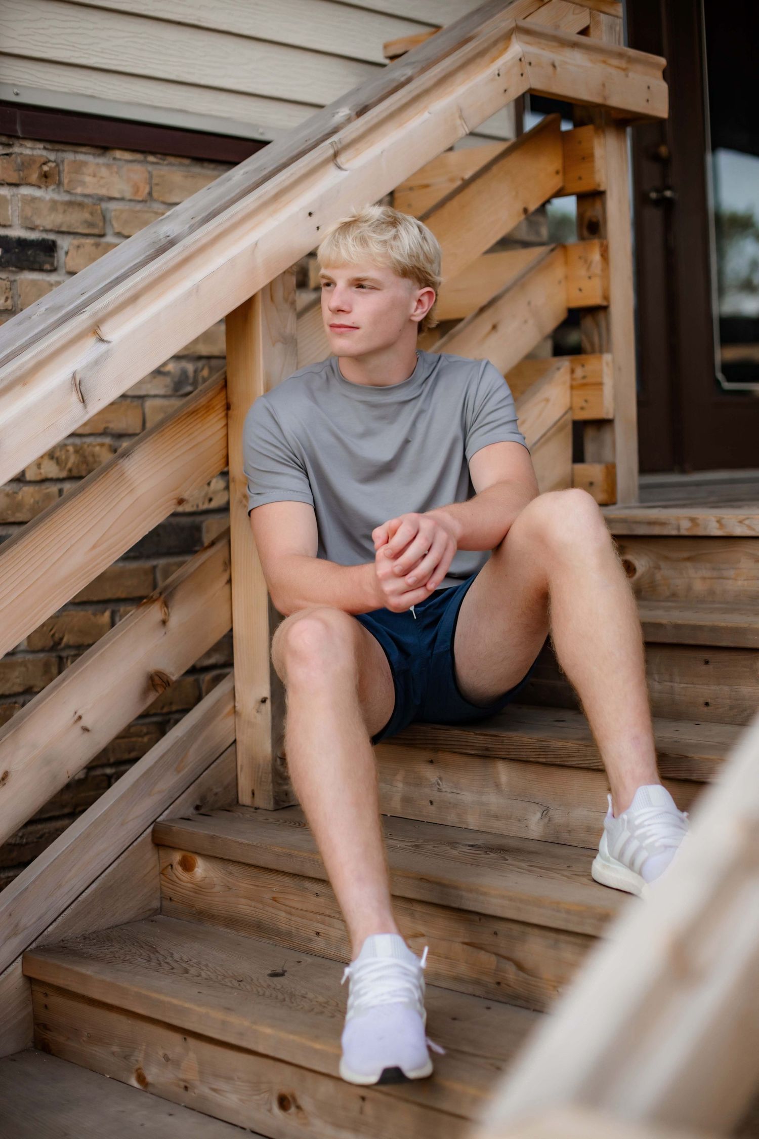 Person in gray t-shirt and shorts sitting casually on wooden stairs outdoors.