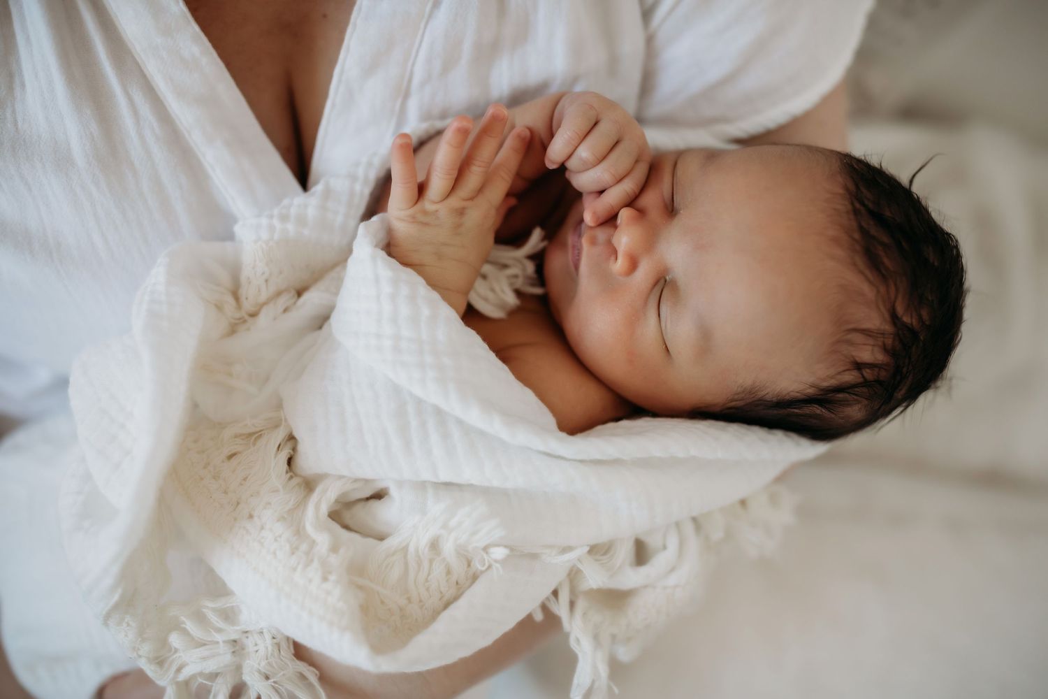 Newborn baby wrapped in white textured blanket sleeping peacefully.