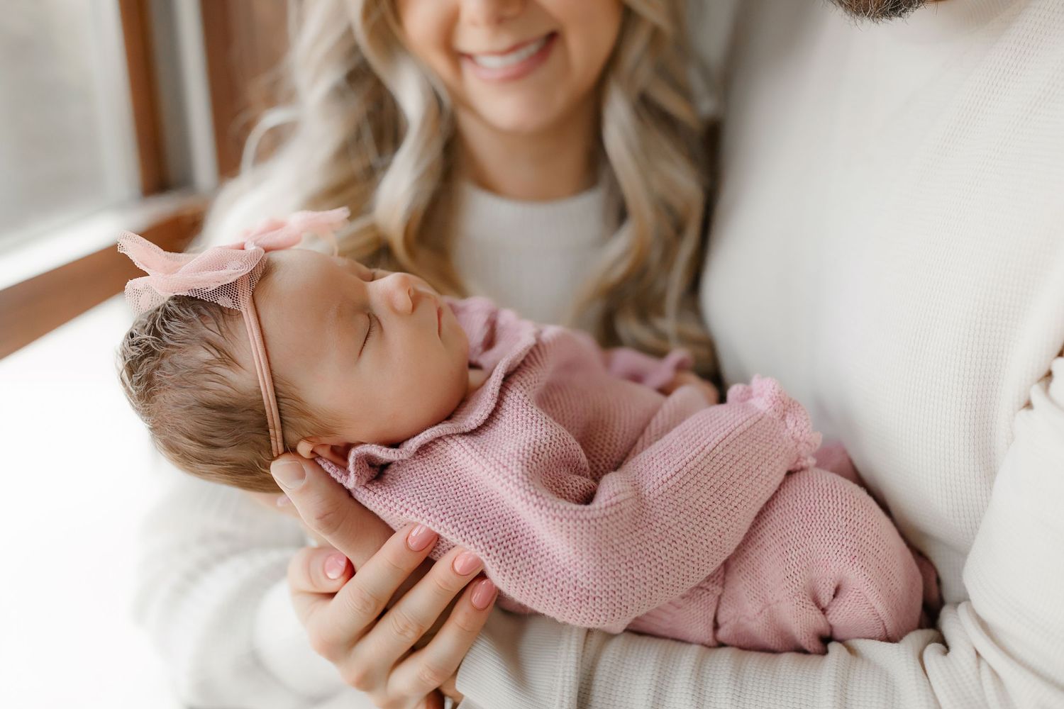 Newborn in pink sweater sleeping peacefully in caring arms.