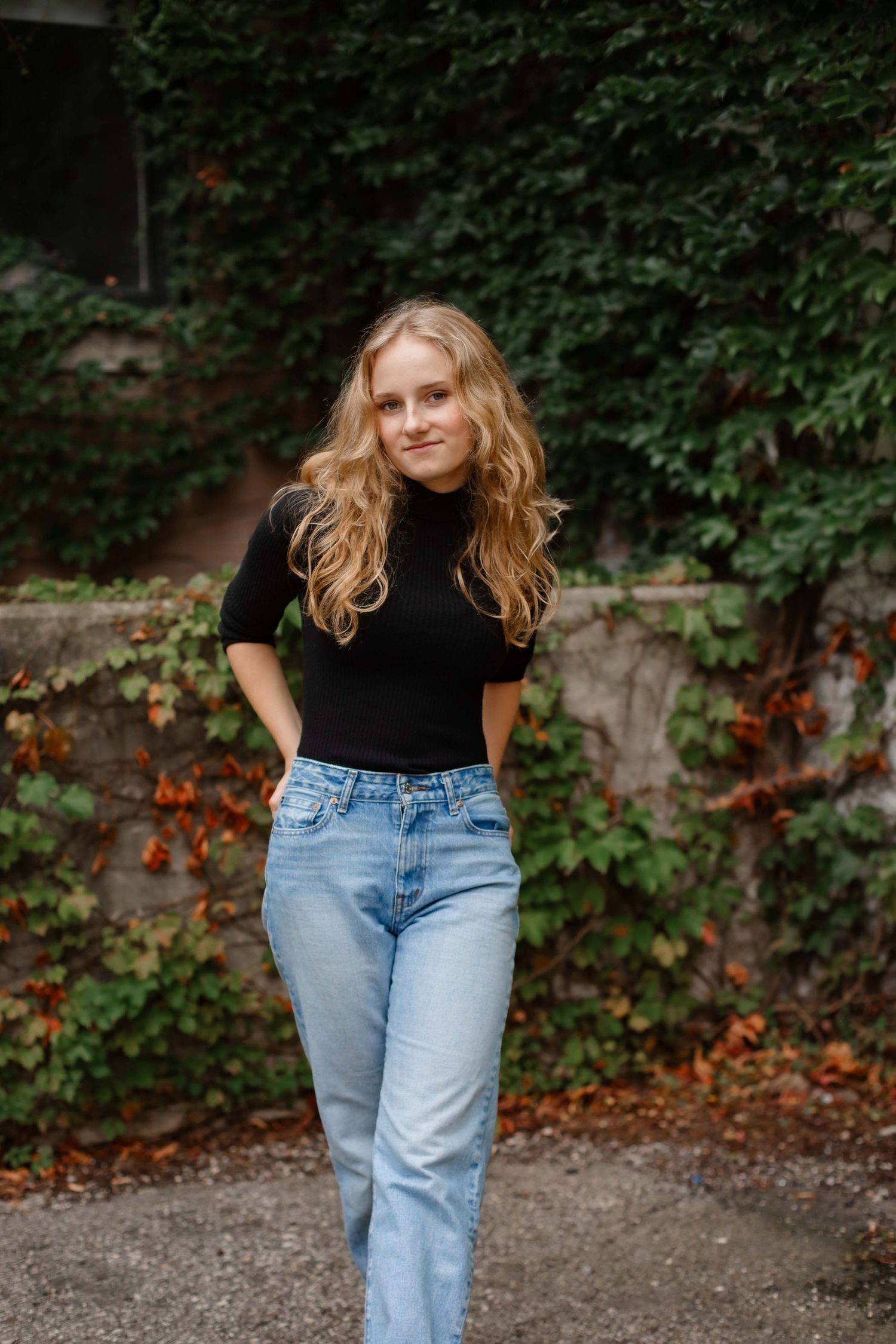 Classic fall fashion look with black turtleneck and light wash jeans against an ivy-covered wall.