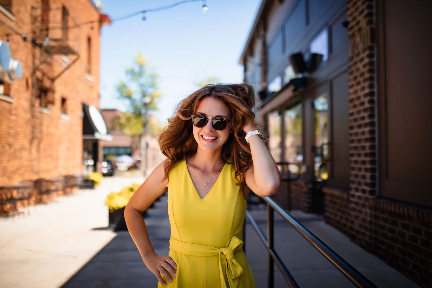 Woman in yellow dress twirls playfully on sunny brick-lined street.