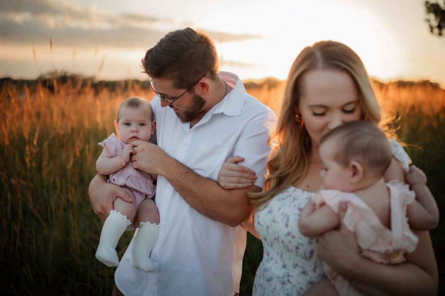 Parents holding twin babies in a field during sunset.