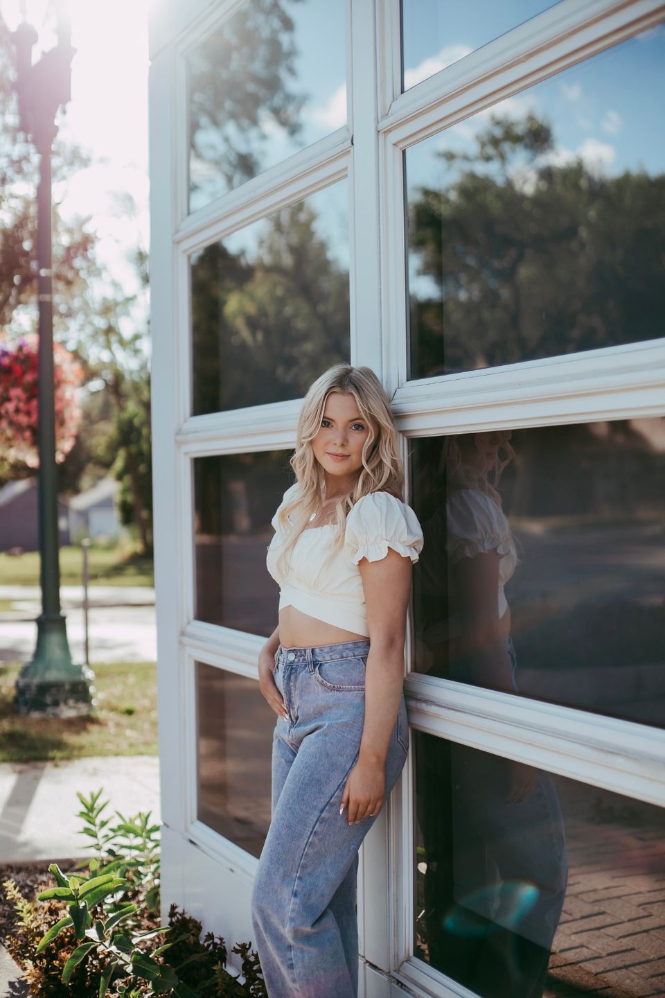 Fashion portrait against a modern glass window wall wearing distressed denim and a white crop top.