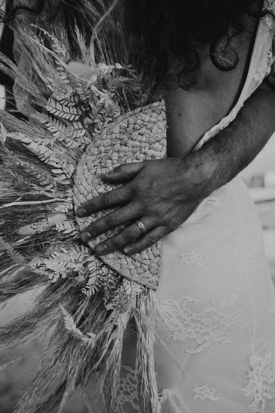 Close-up black and white detail of woven grass bouquet against lace dress.