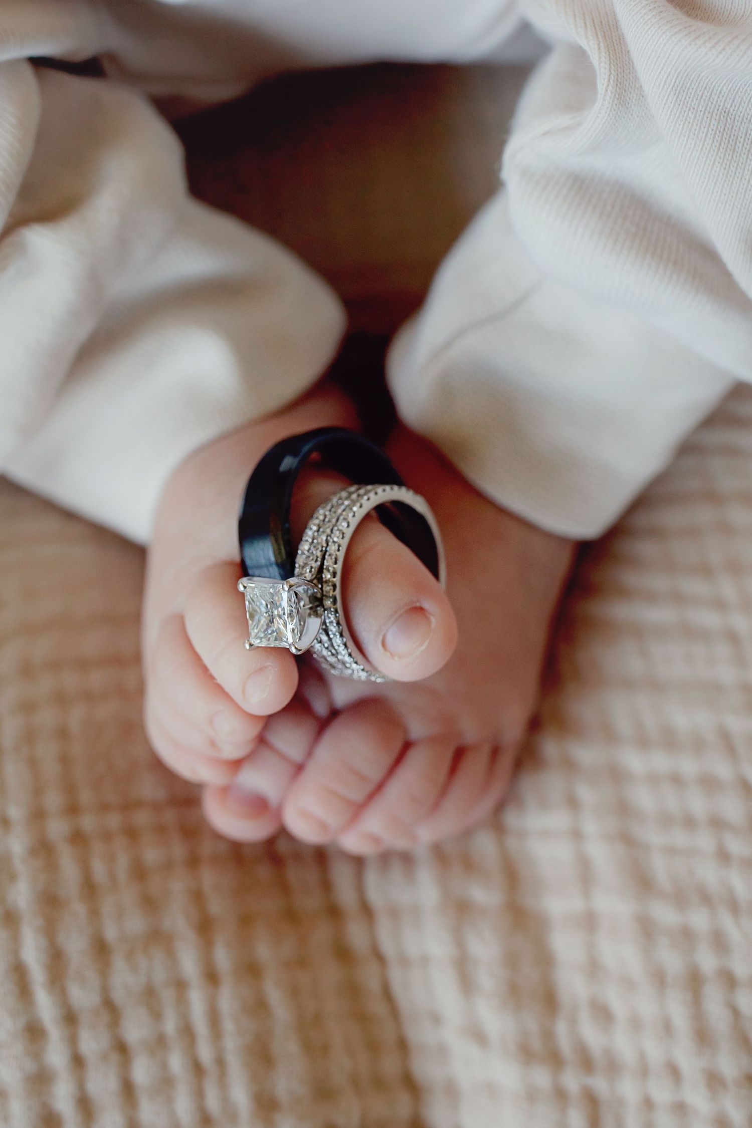 Close-up of tiny baby feet with a sparkling diamond engagement ring balanced between the toes.