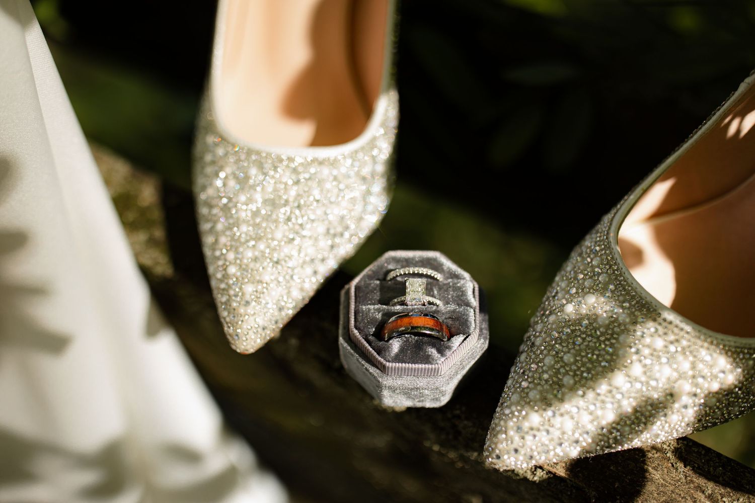 A close-up of sparkling silver wedding rings and jewelry displayed on a textured white surface in natural light.