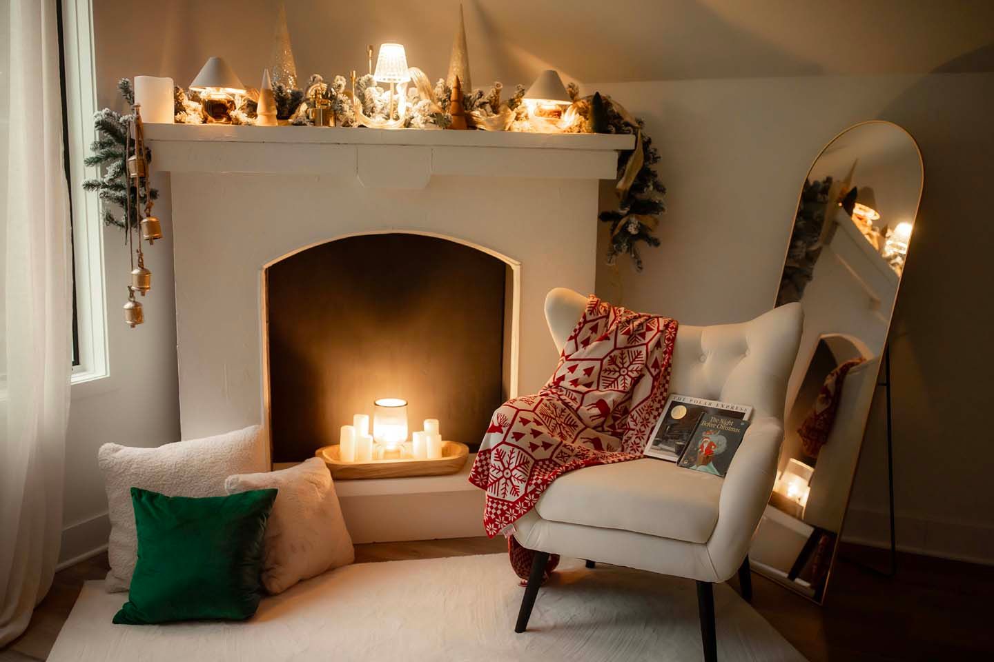 Cozy Christmas living room with lit fireplace, candles, white armchair with red throw, green pillow, and festive mantel decor.