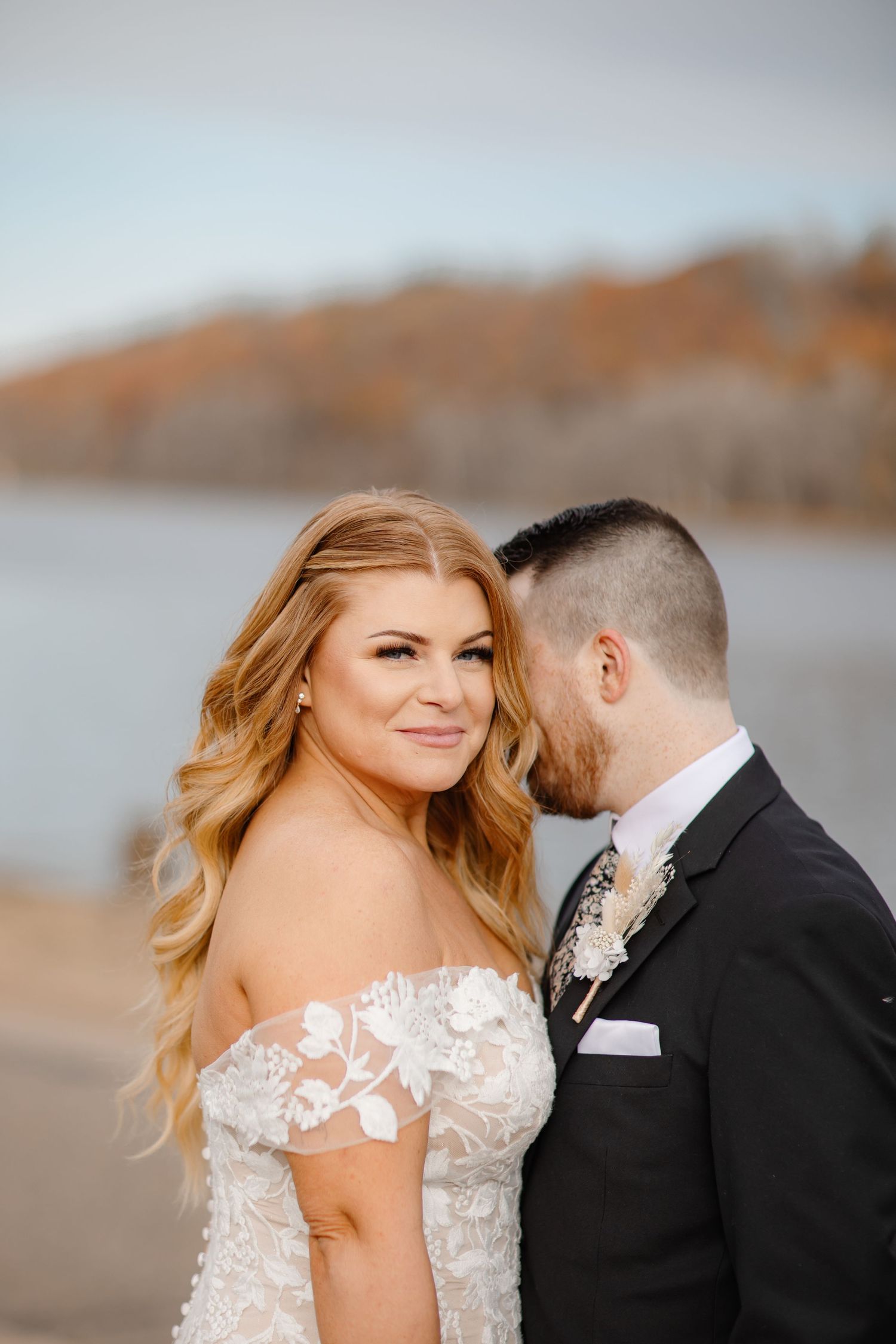 Newlyweds share a tender moment by a lake during their autumn wedding photoshoot.
