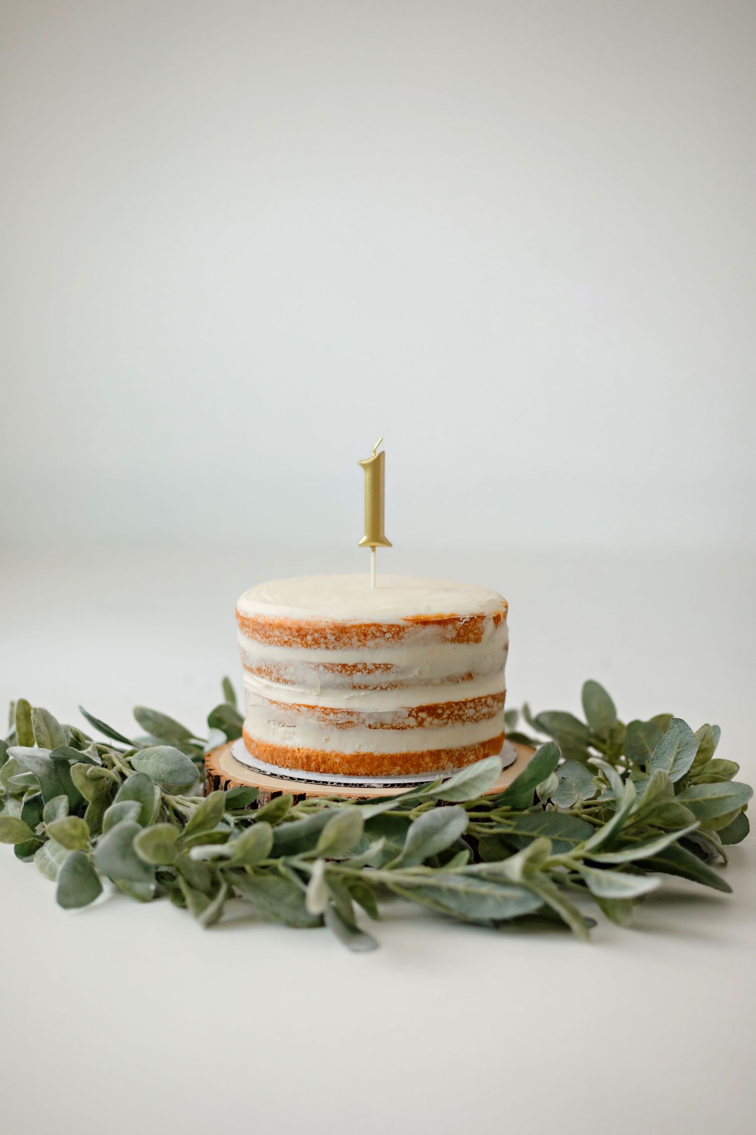 Naked cake with gold number one candle surrounded by eucalyptus garland.
