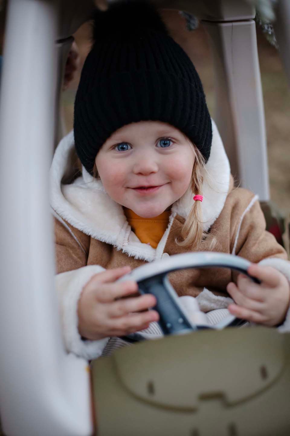 Young child in winter hat and coat sitting in toy car.