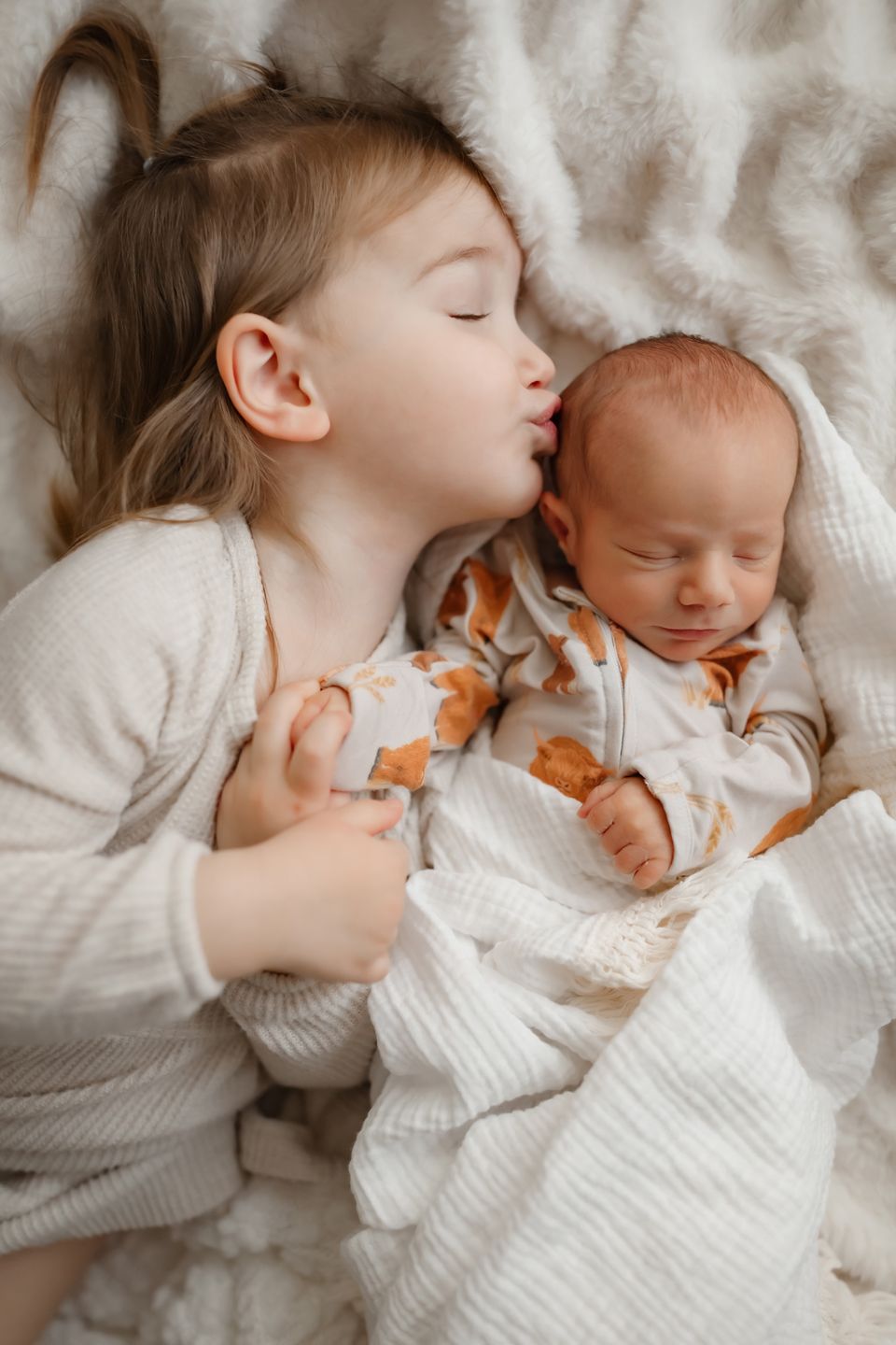Sweet bonding moment between siblings laying together on white bedding.