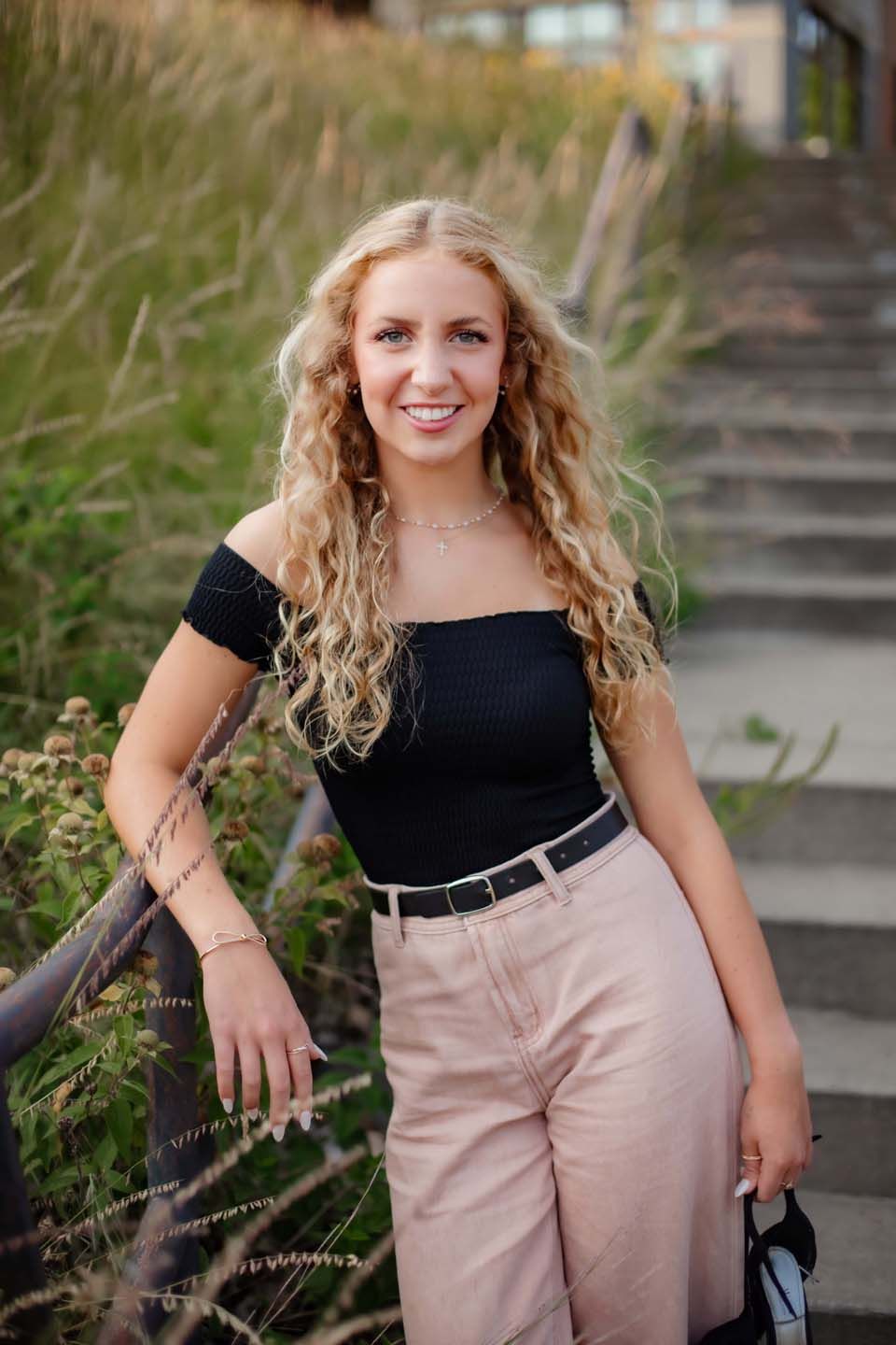 Outdoor fashion portrait on steps with natural grasses featuring black top and pink pants.