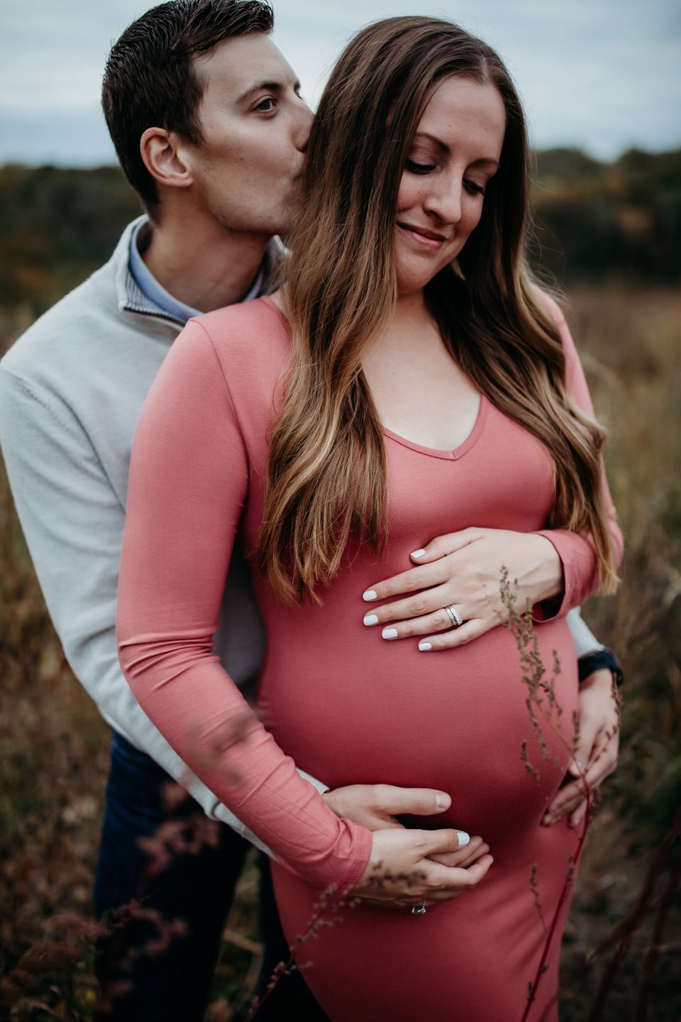 Intimate maternity moment with couple in pink and gray clothing outdoors.