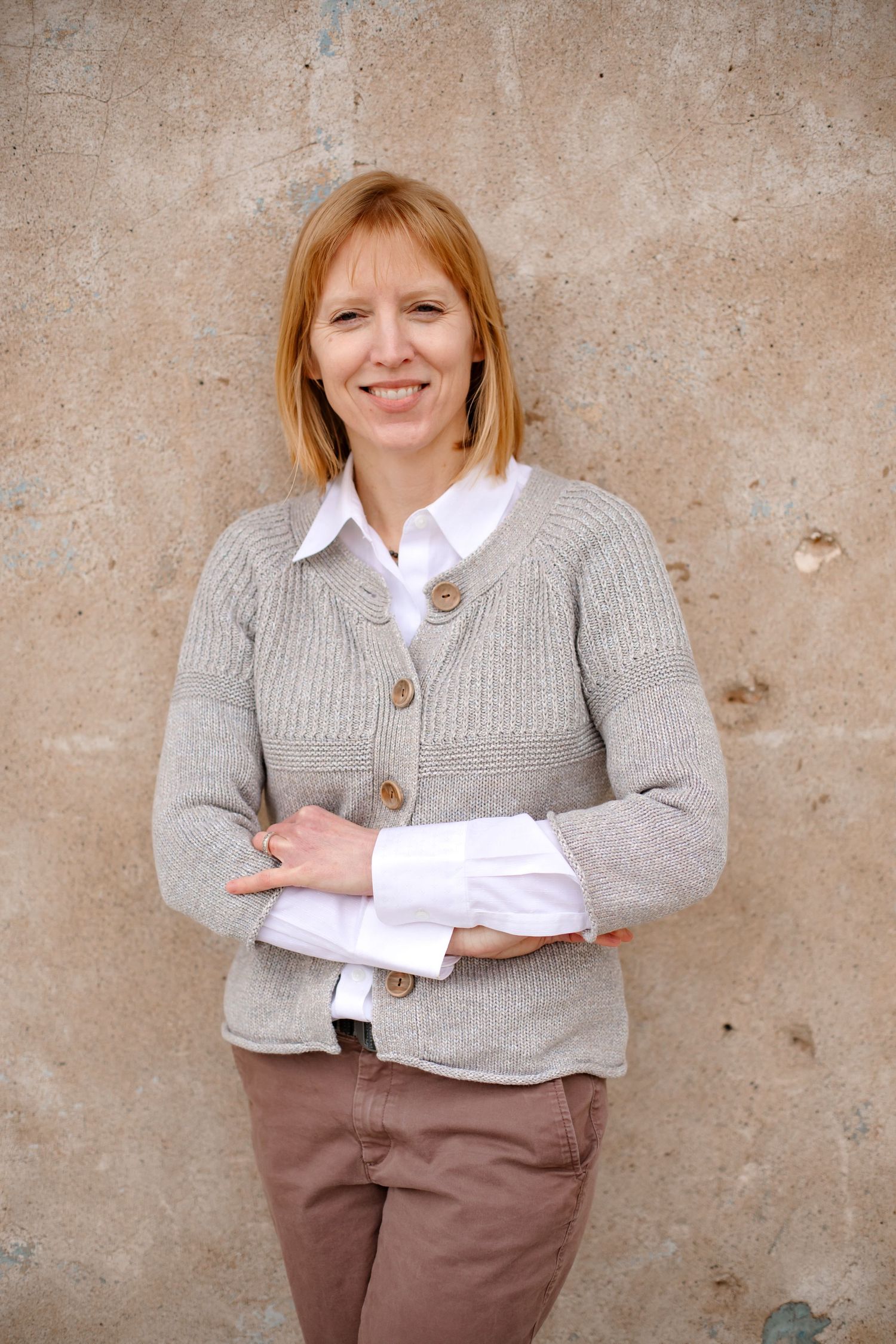 Casual business attire with gray cardigan and white shirt against textured wall.
