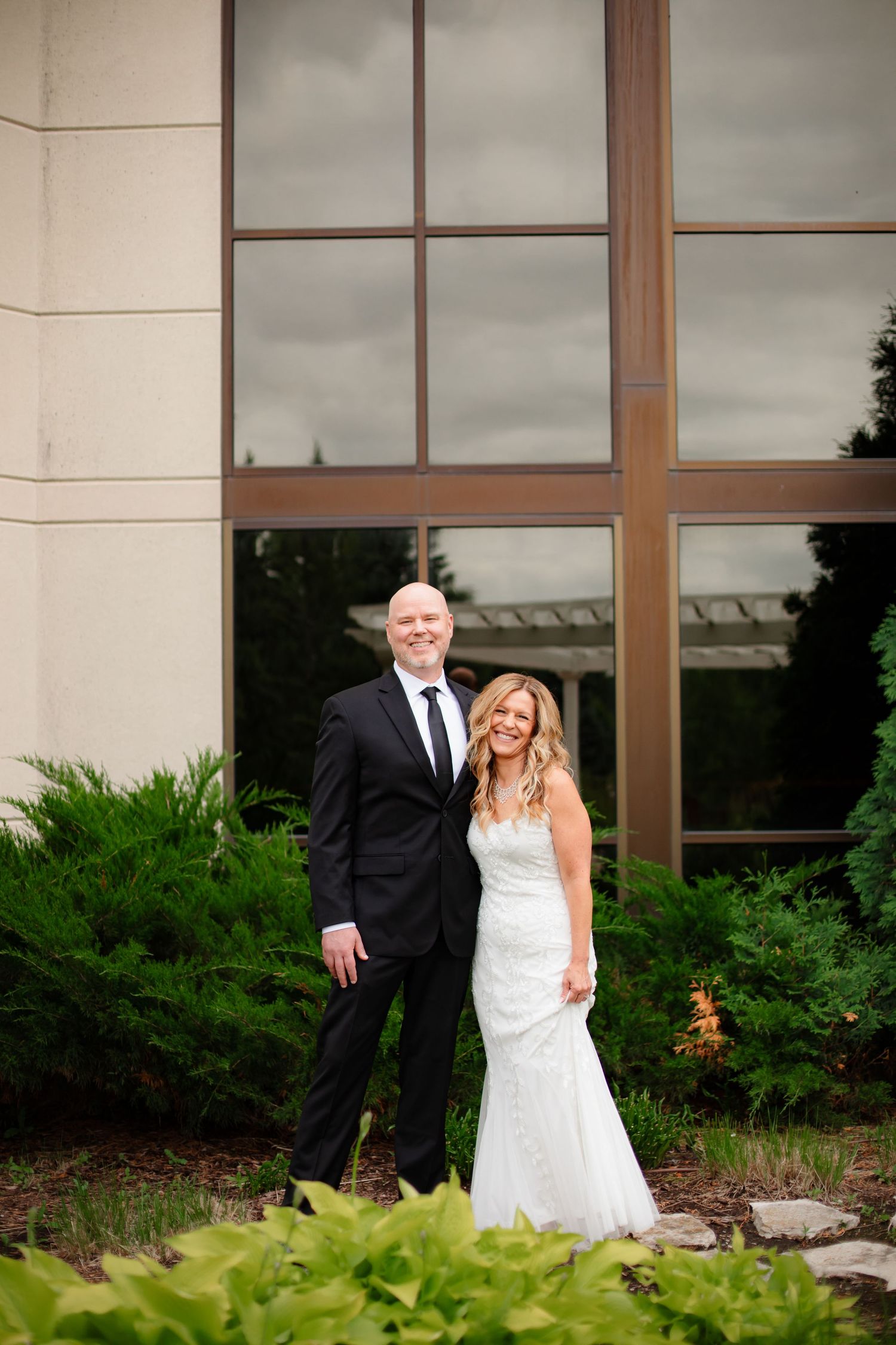 A series of candid wedding photos showing playful moments between a couple against a building exterior with greenery.