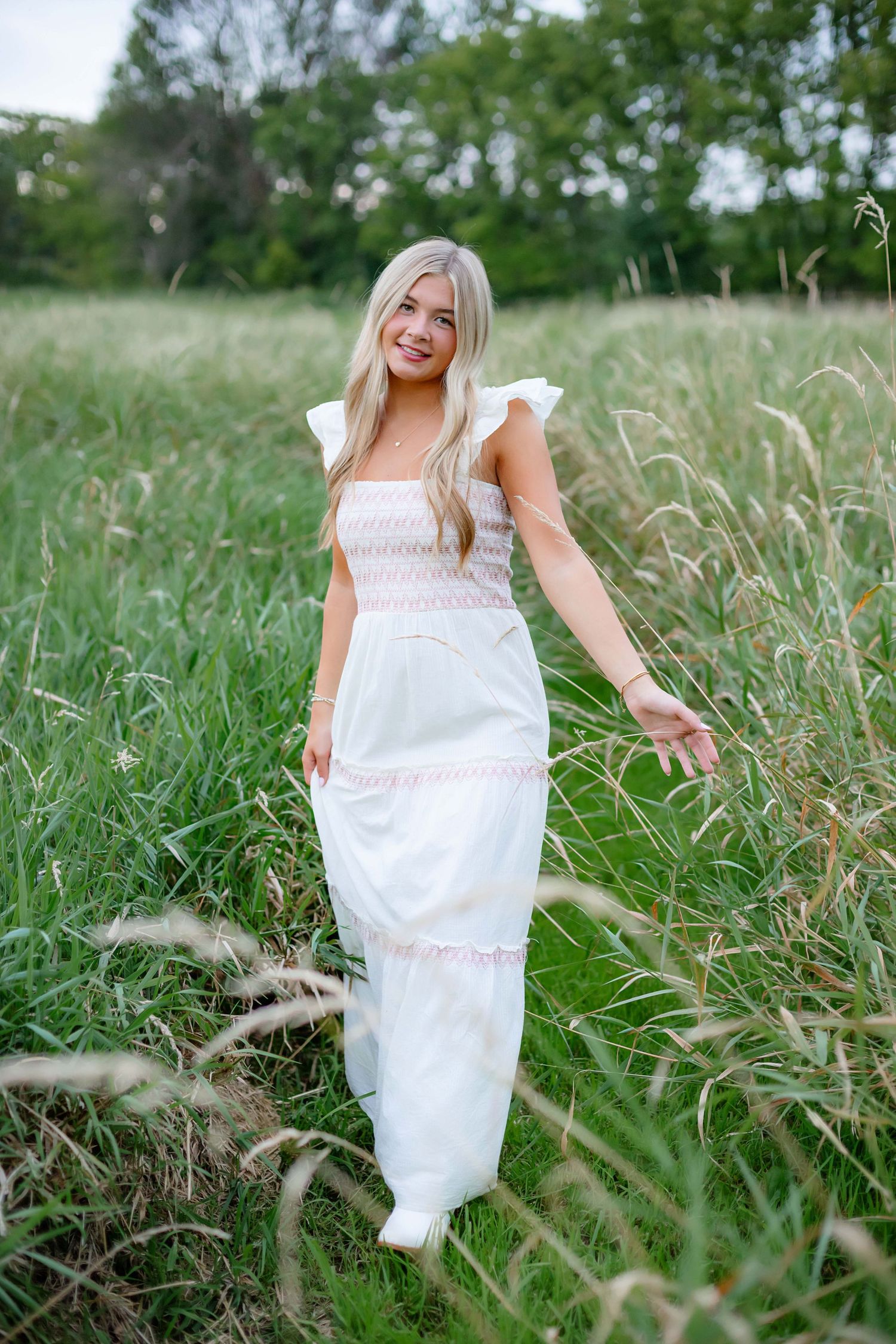 Outdoor photoshoot in a flowing white summer dress among tall grass in a natural field setting.