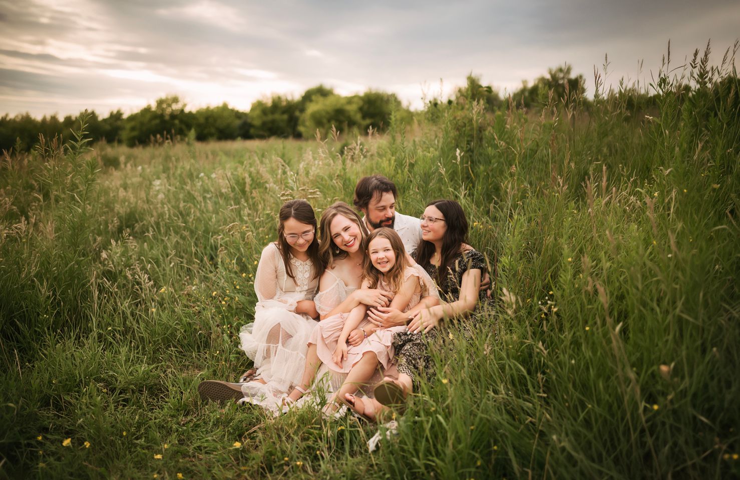 Happy family of six sitting together in a lush green meadow field during golden hour outdoor portrait. Willow & Wren Photography Chaska, mn