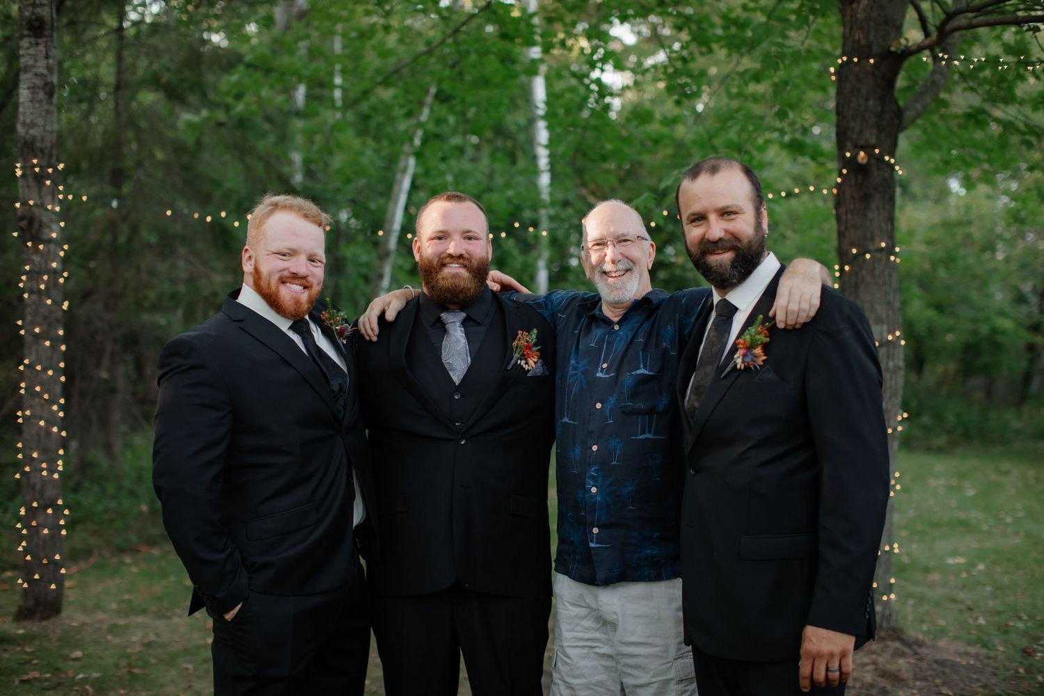 Groomsmen in dark suits pose together in casual outdoor wedding photo.