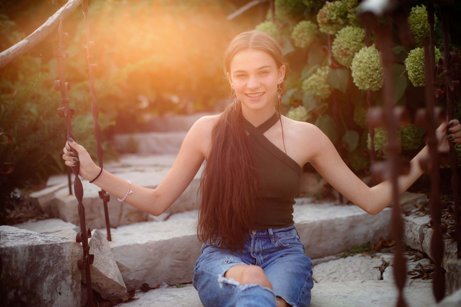 Relaxed outdoor portrait on stone steps surrounded by lush greenery at sunset.