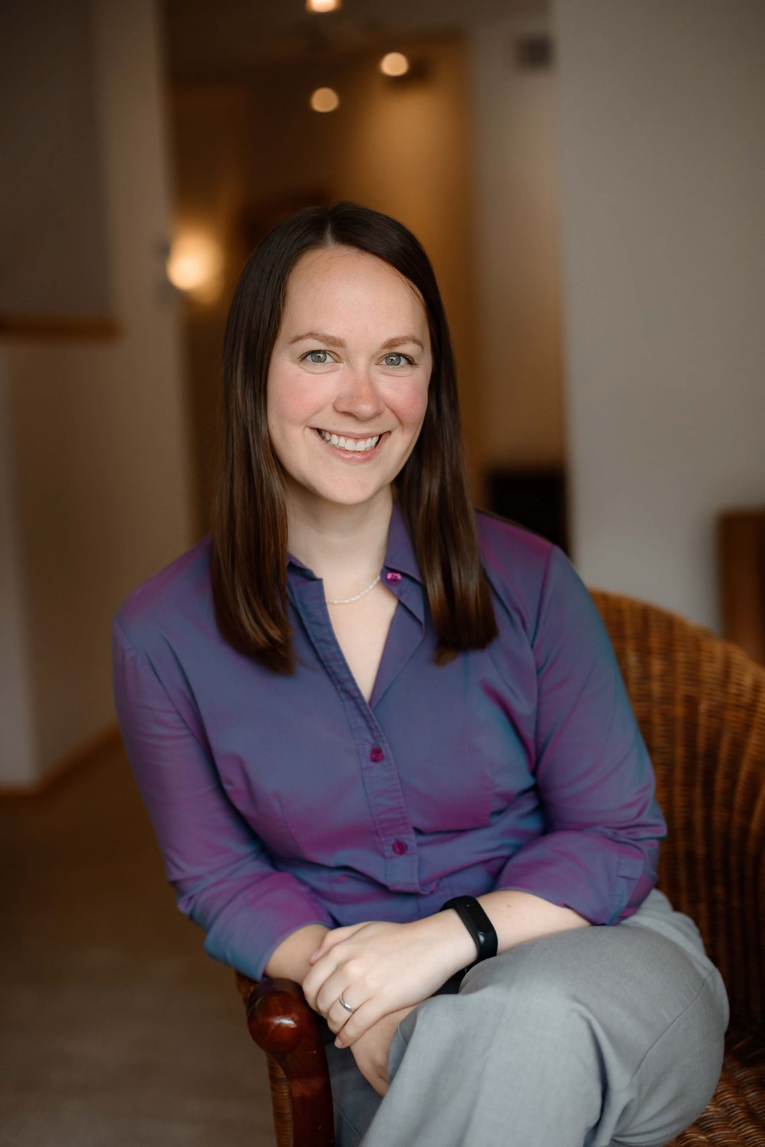 Professional portrait of woman in purple top seated in wooden chair.