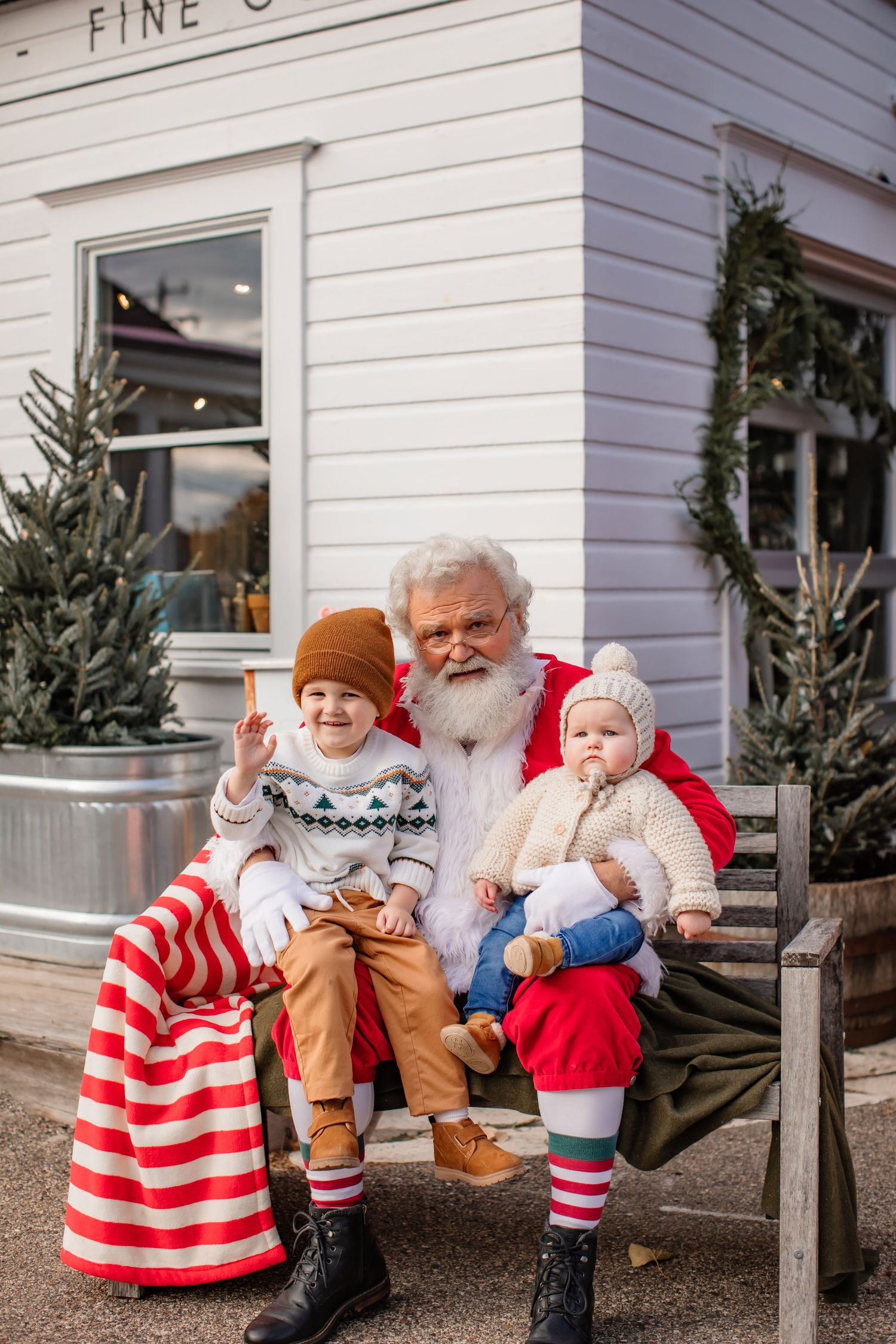 Christmas scene outside white building with striped decorations and evergreen trees.
